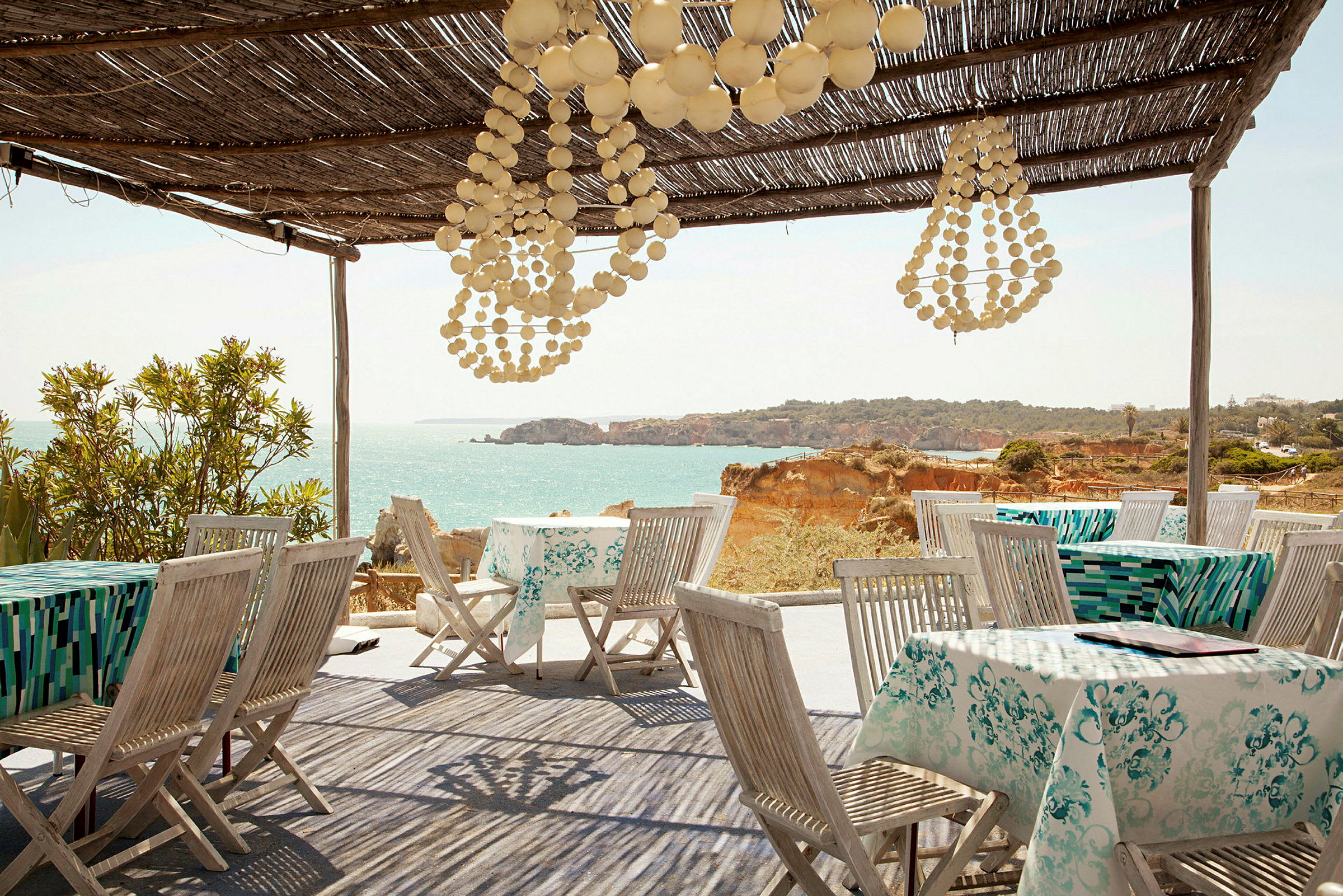 Restaurant med utsikt mot havet, bord dekket med duker og tremøbler under et tak av tre. (AI-generert tekst)