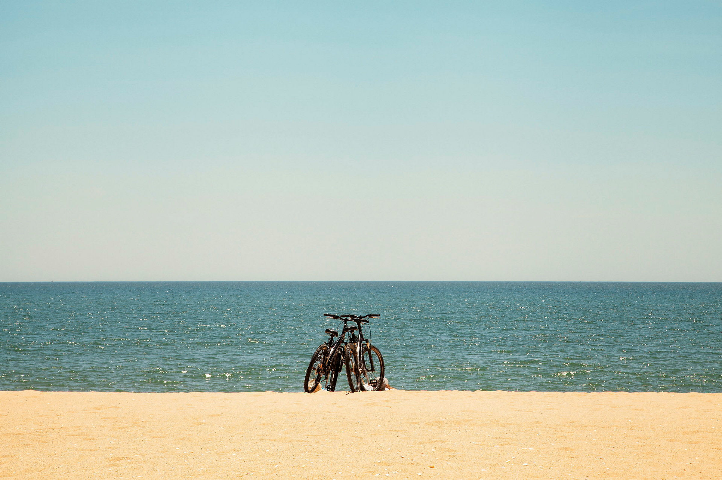 To sykler står på en sandstrand med havet i bakgrunnen. (AI-generert tekst)