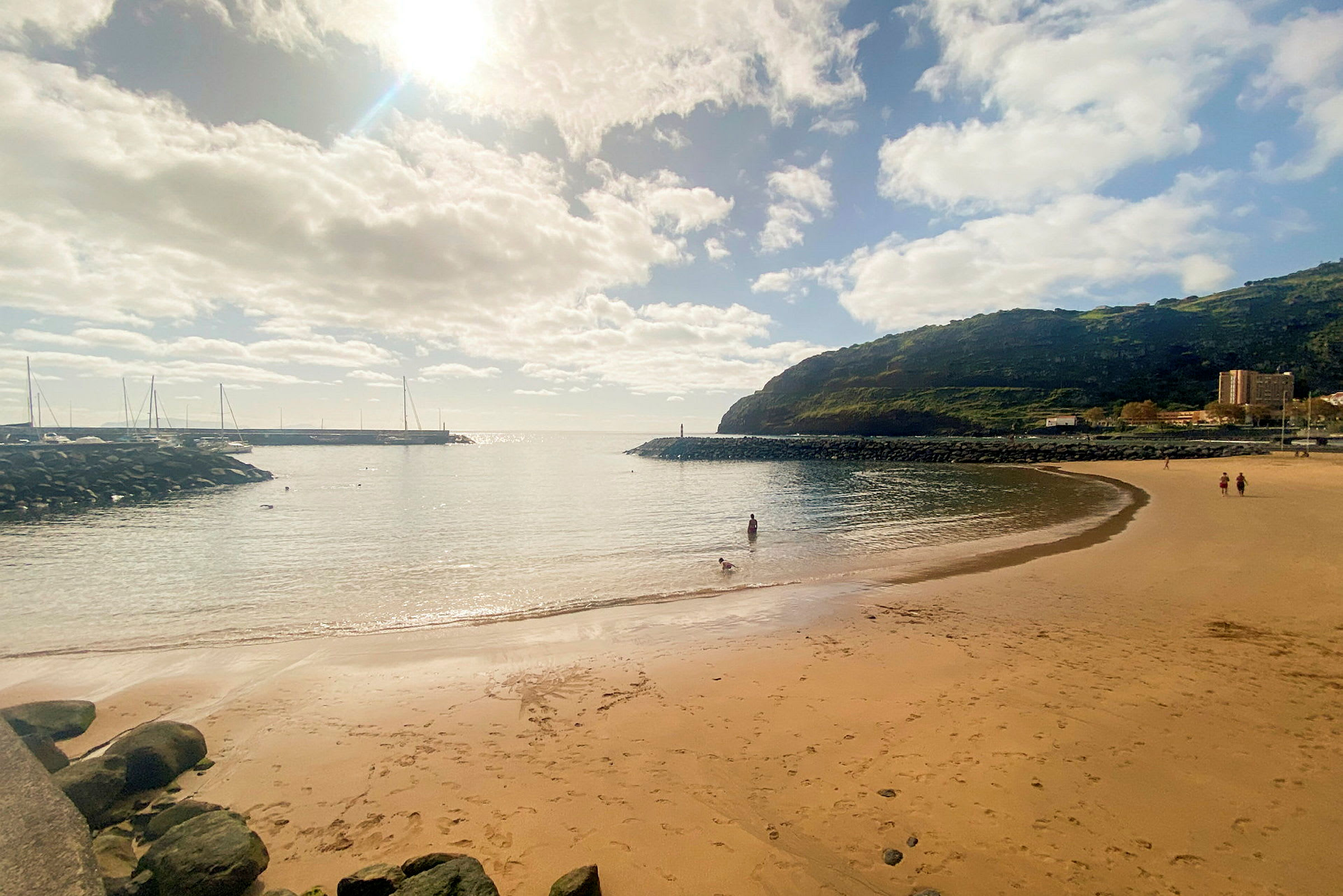 En sandstrand med havet, noen mennesker og en frodig ås i bakgrunnen. (AI-generert tekst)
