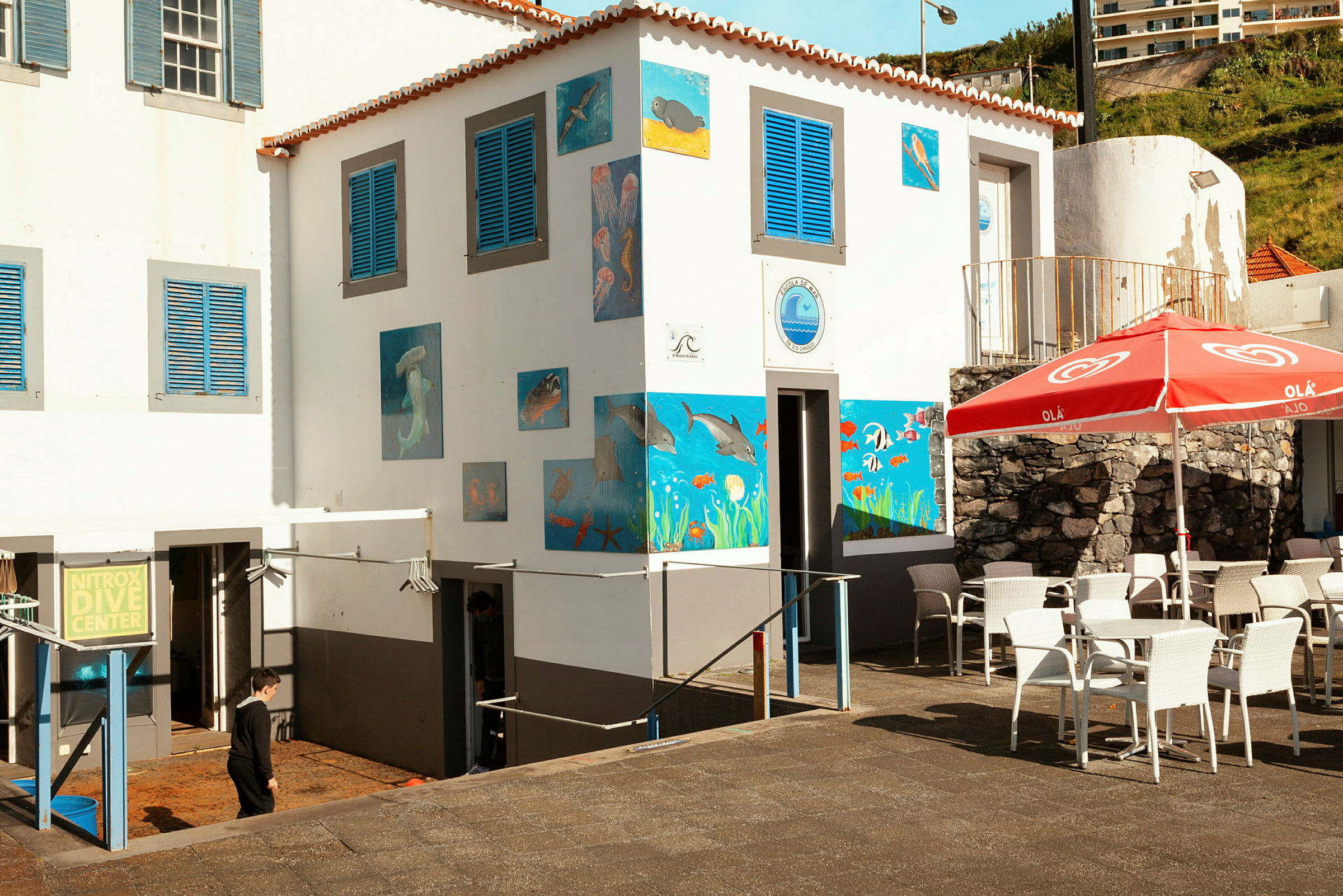 Dykkesenter med fargerike undervannsmalerier og uteservering med bord og stoler. (AI-generert tekst)
