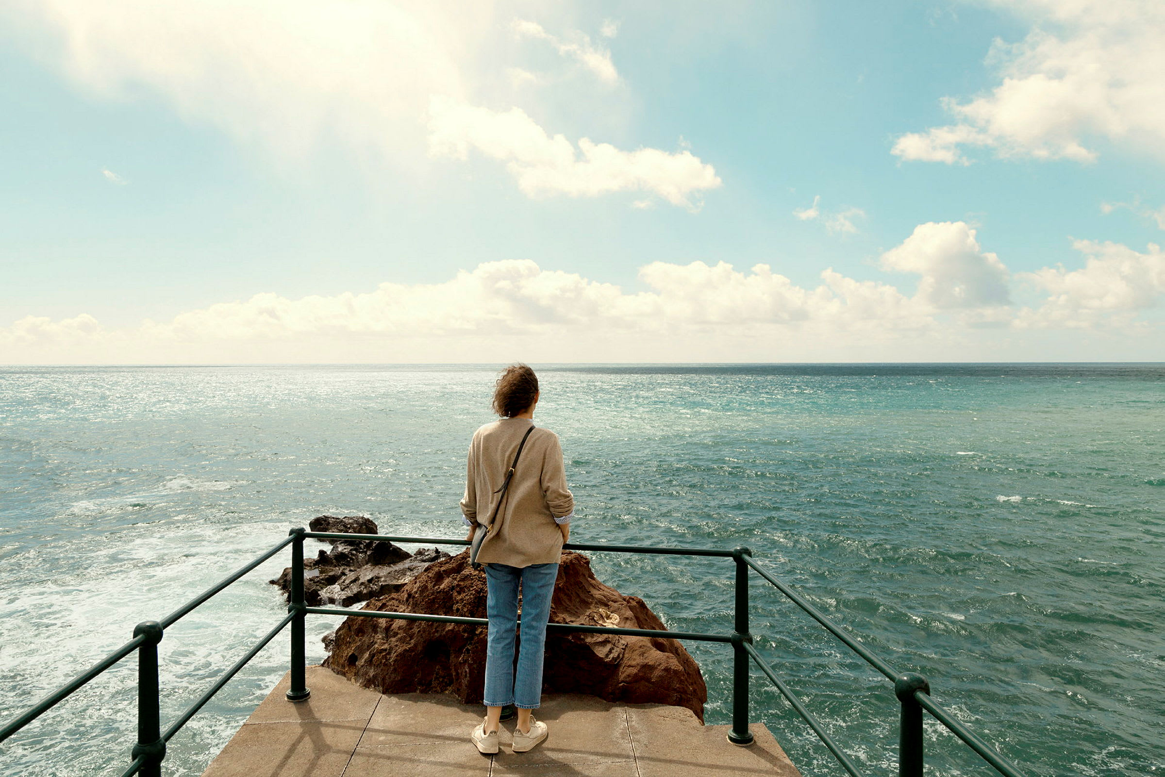 En person står på et utsiktspunkt og ser ut over havet. (AI-generert tekst)