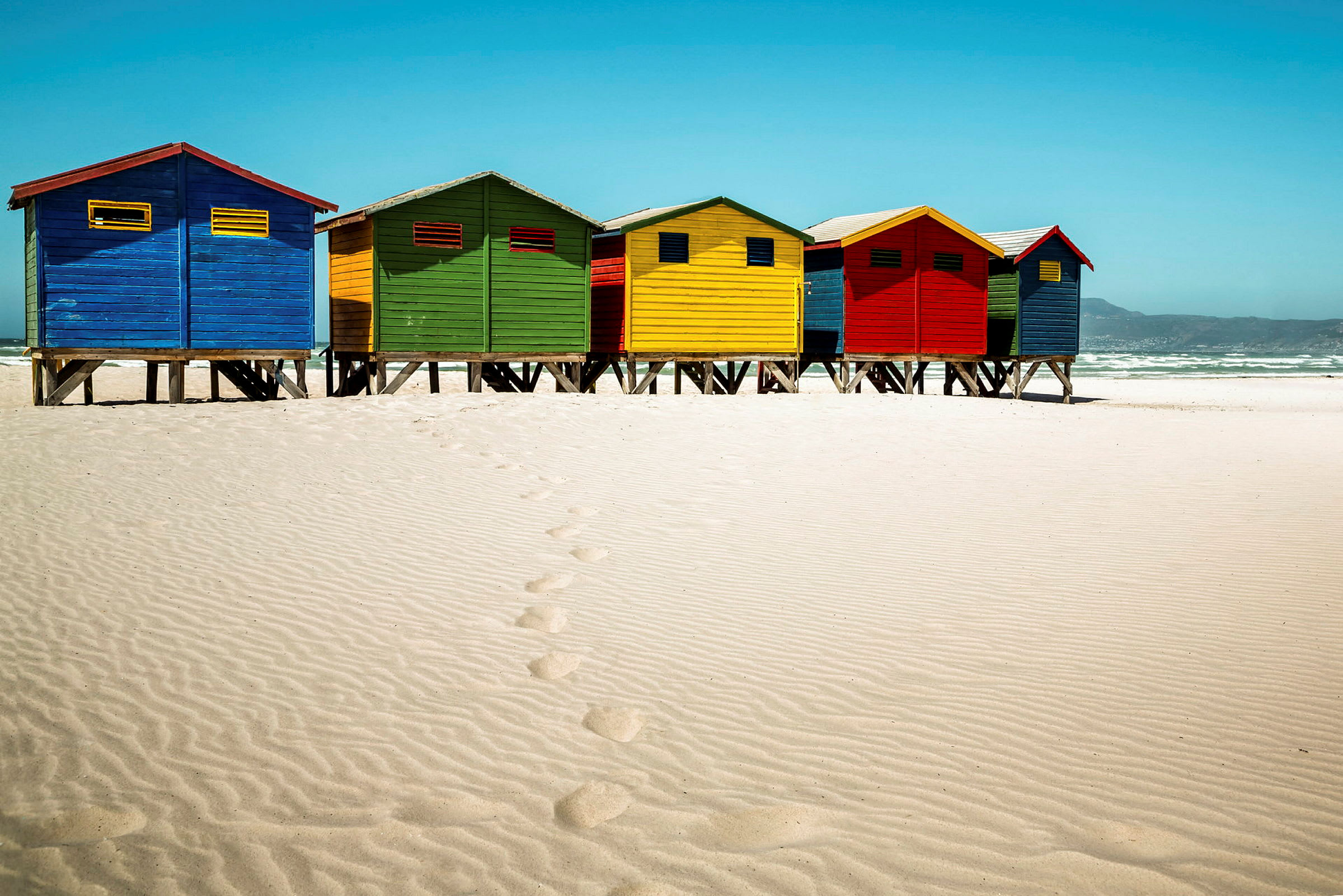 Fargerike strandhytter på en sandstrand. (AI-generert tekst)