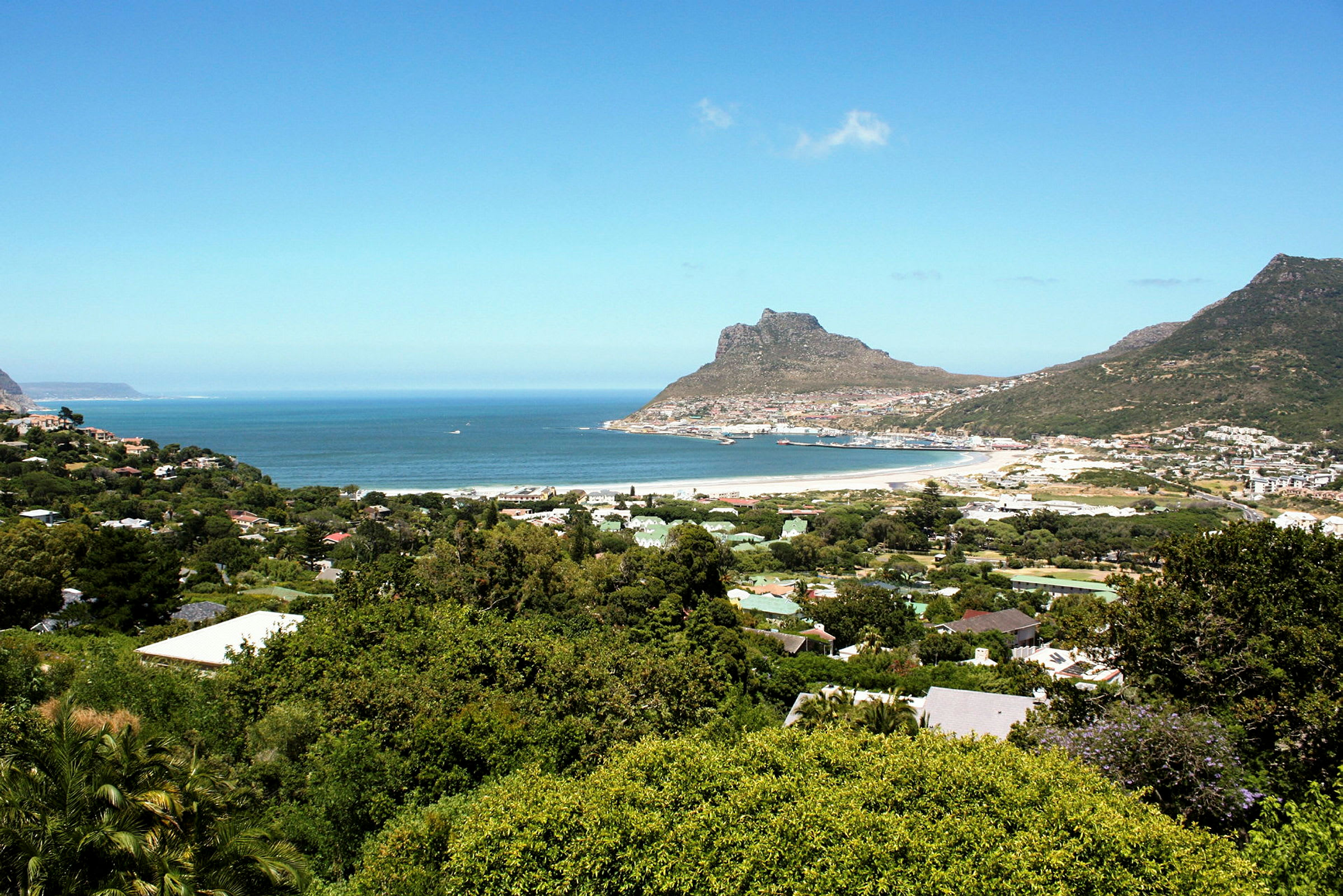 En kystutsikt med hav, sandstrand og omliggende grønt, inkludert fjell i bakgrunnen. (AI-generert tekst)