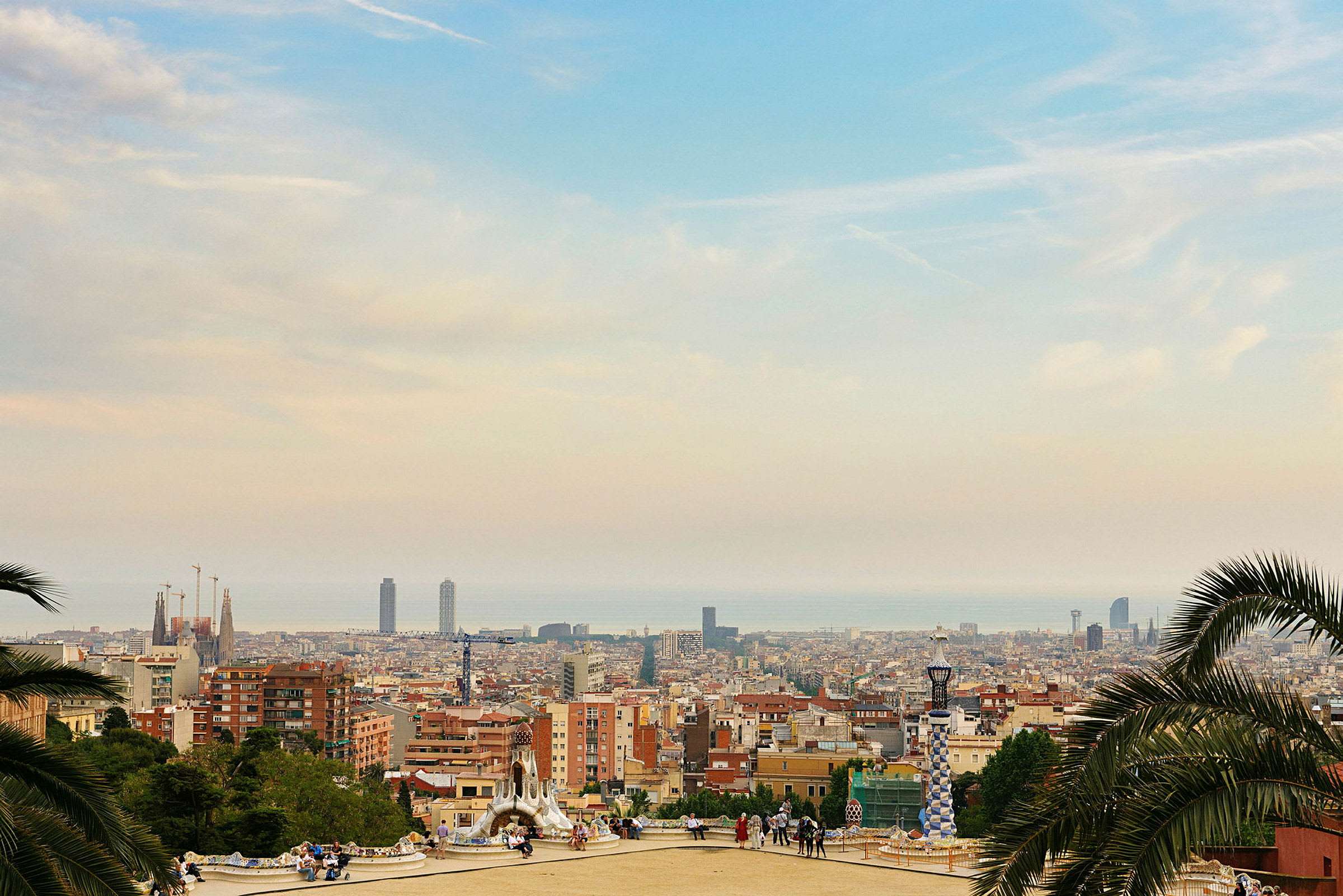 En utsikt over Barcelona fra et høyt punkt, med bygninger, tårn og havet i det fjerne. (AI-generert tekst)