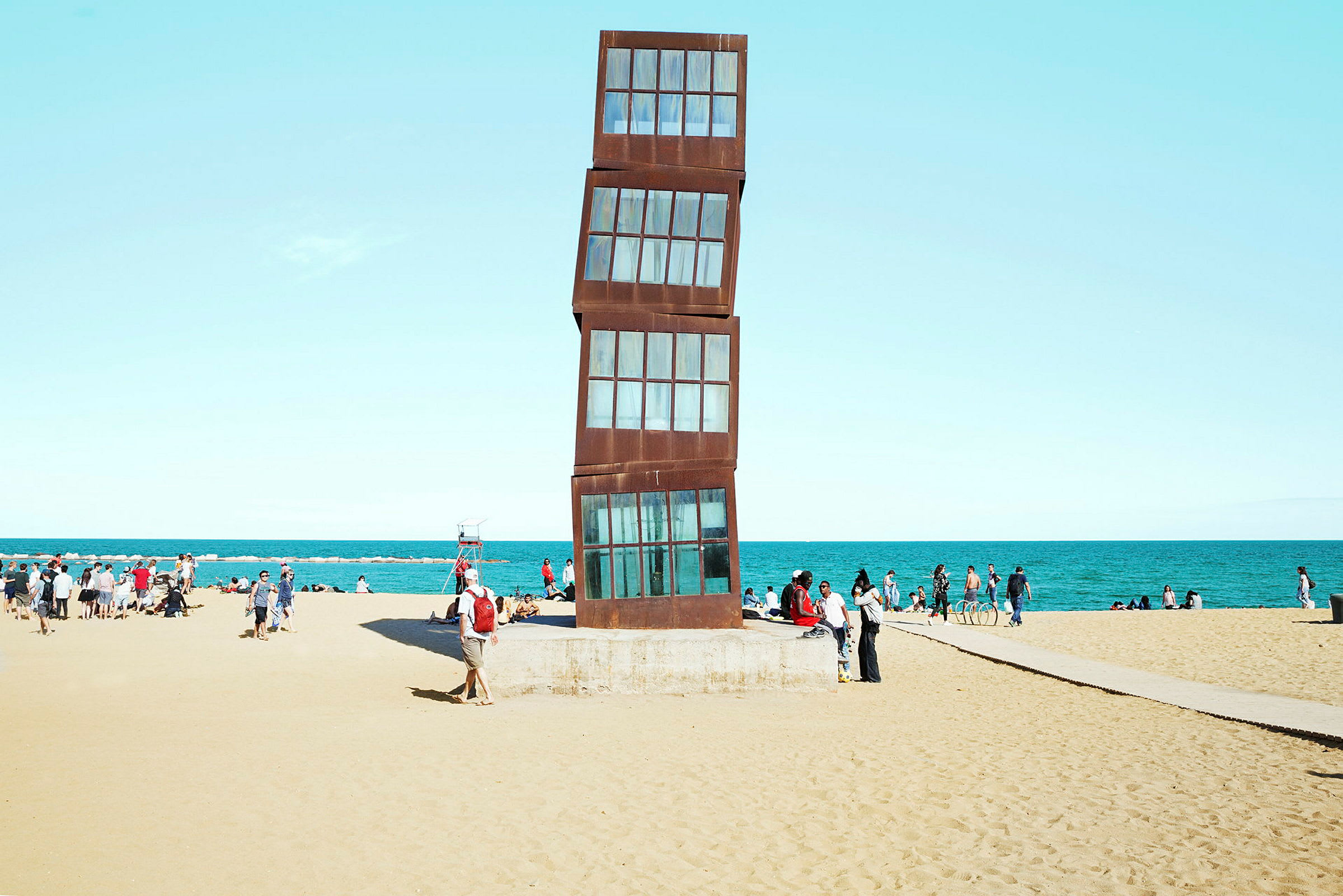 Bilde av en strand med en moderne kunstskulptur i fokus og folk i bakgrunnen. (AI-generert tekst)