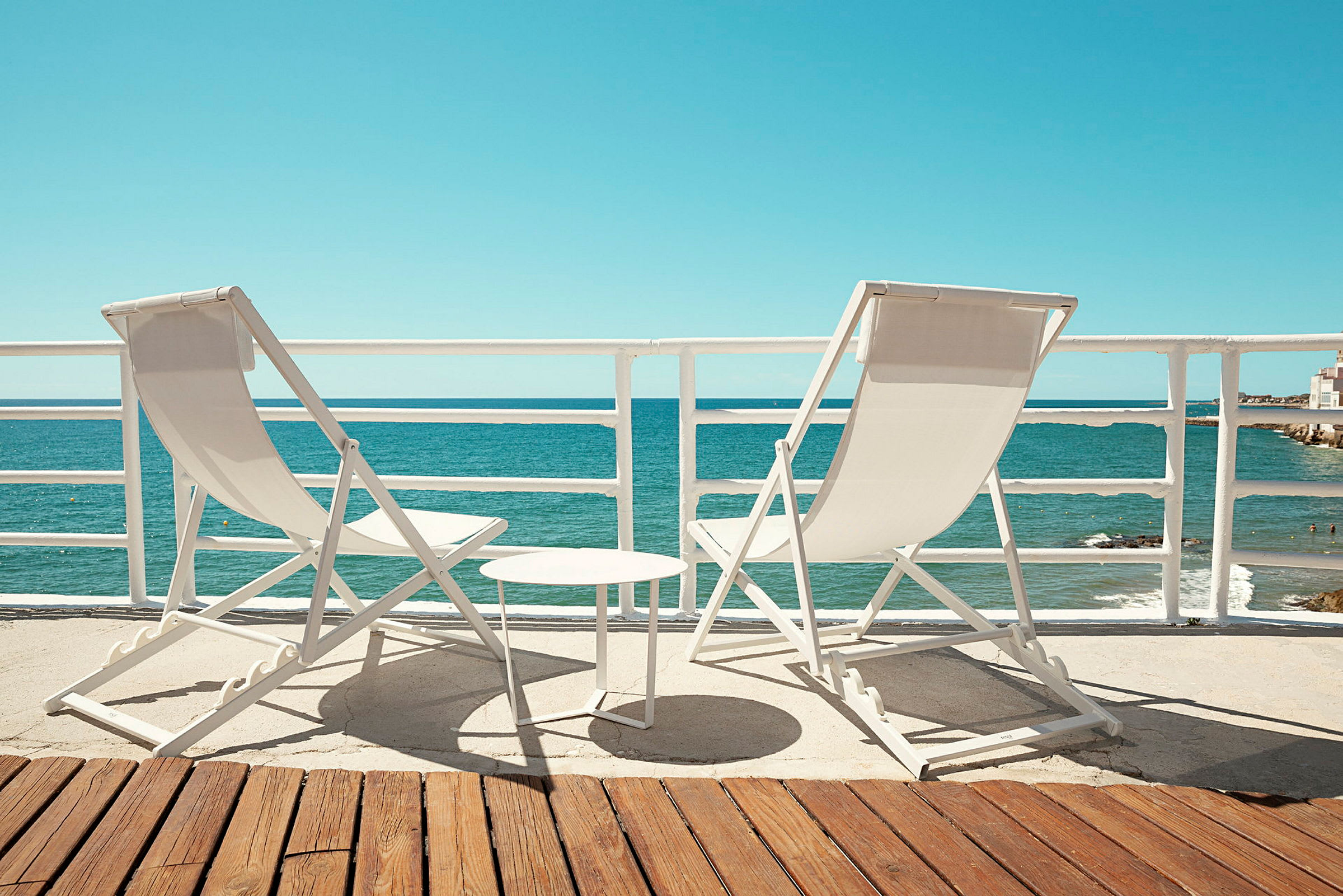 To solstoler og ett lite bord står på en terrasse med utsikt over havet. (AI-generert tekst)