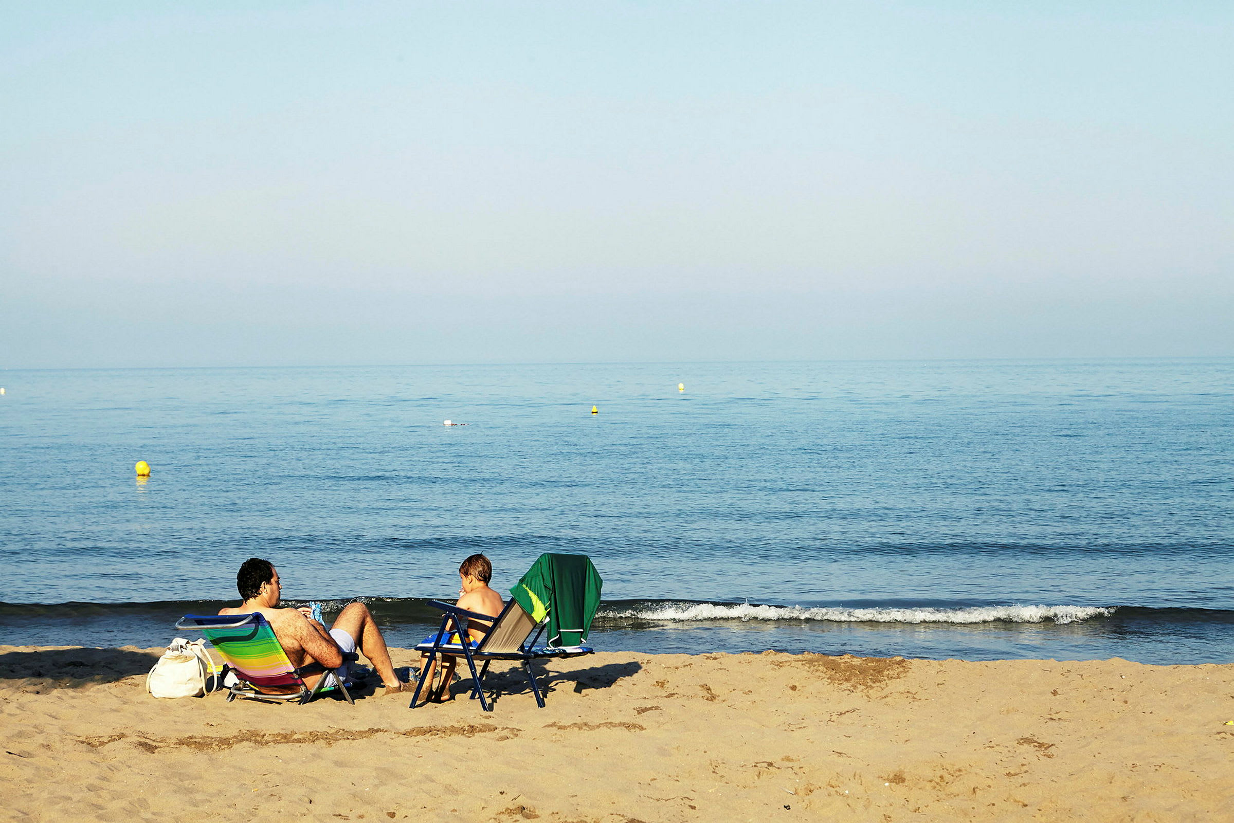 To personer sitter i strandstoler på en sandstrand og ser på havet. (AI-generert tekst)