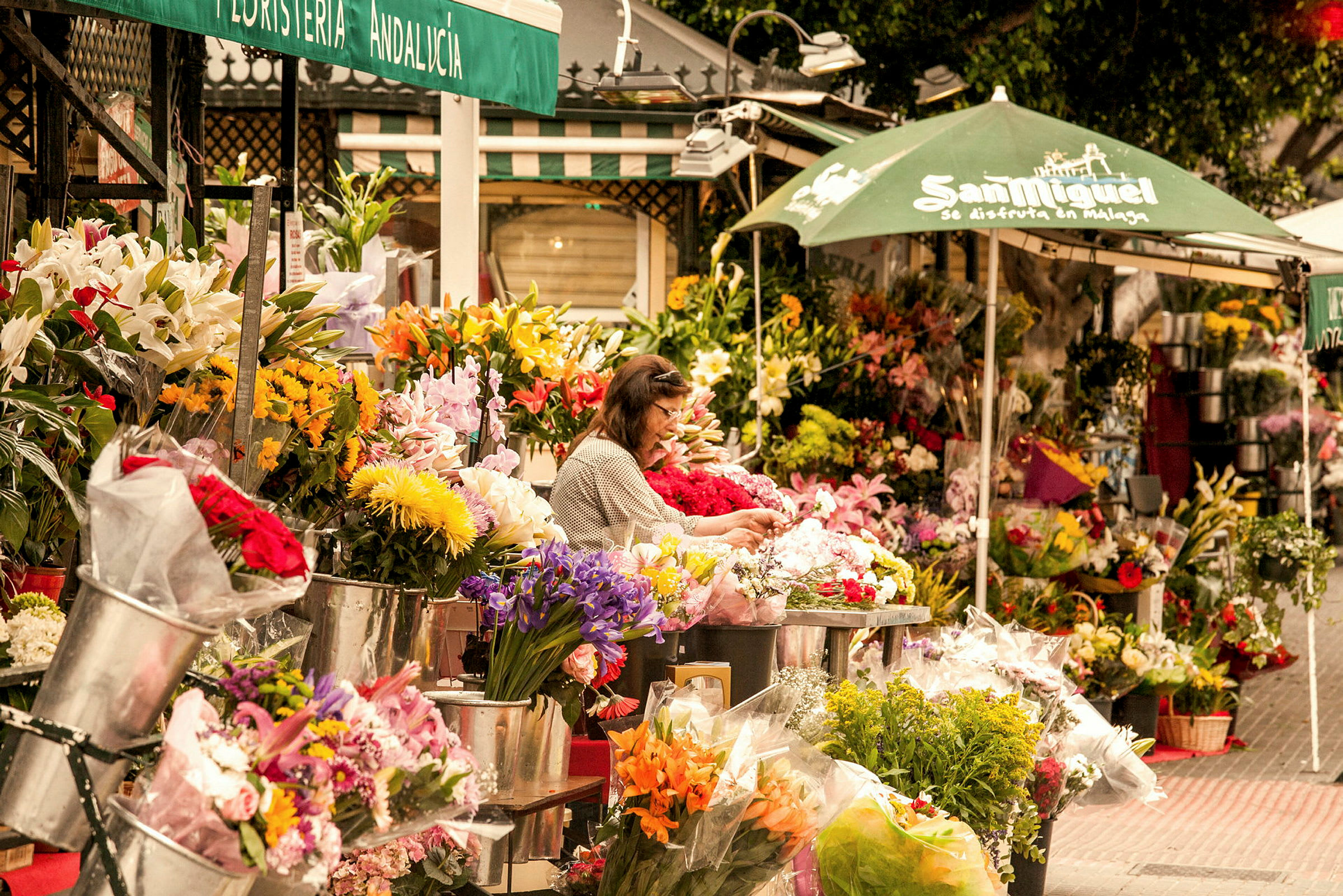 Blomsterstativ på en gate med ulike fargerike buketter og oppsatser, samt en person som forbereder blomster. (AI-generert tekst)