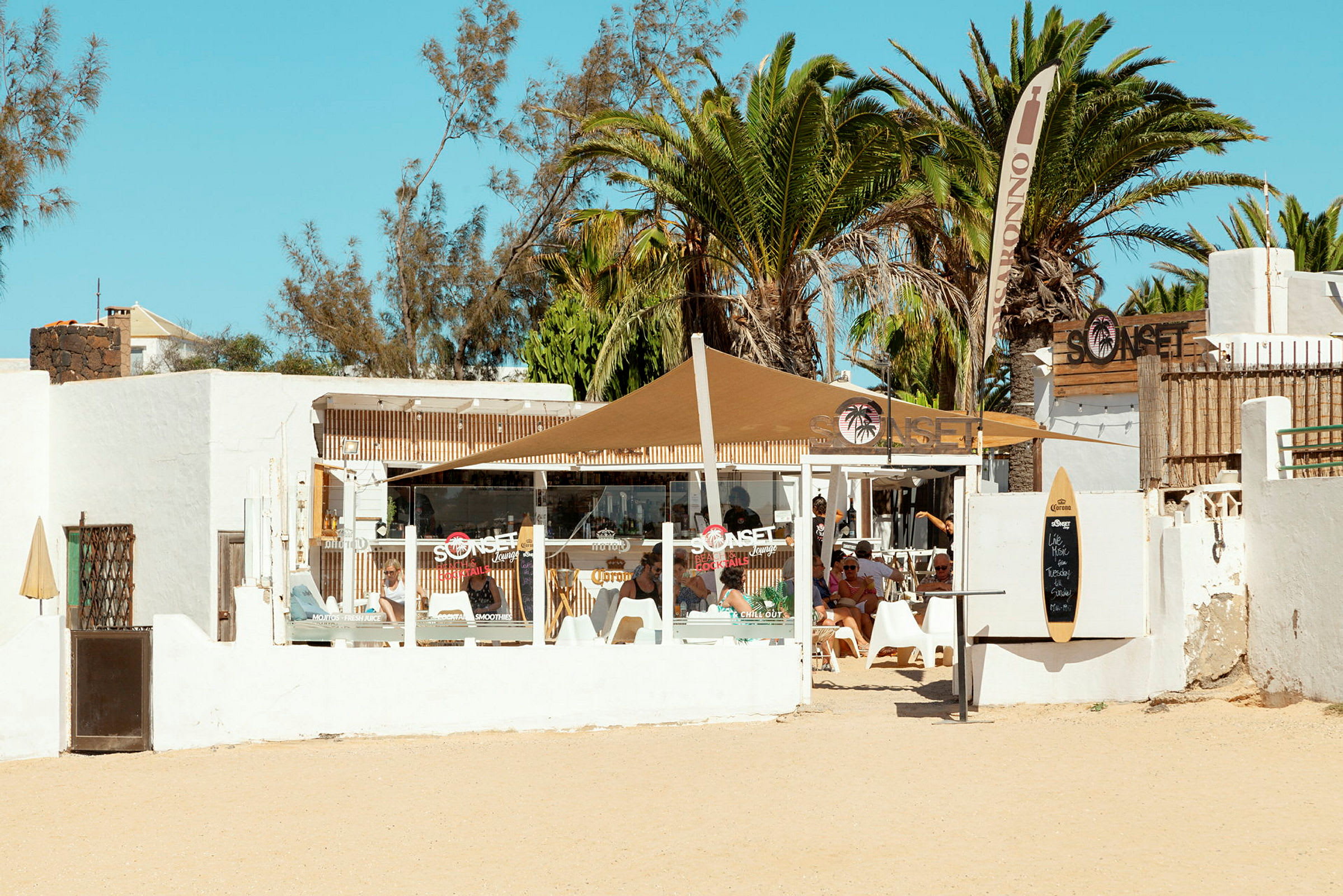 En strandkafé med hvite vegger og palmer i bakgrunnen. (AI-generert tekst)