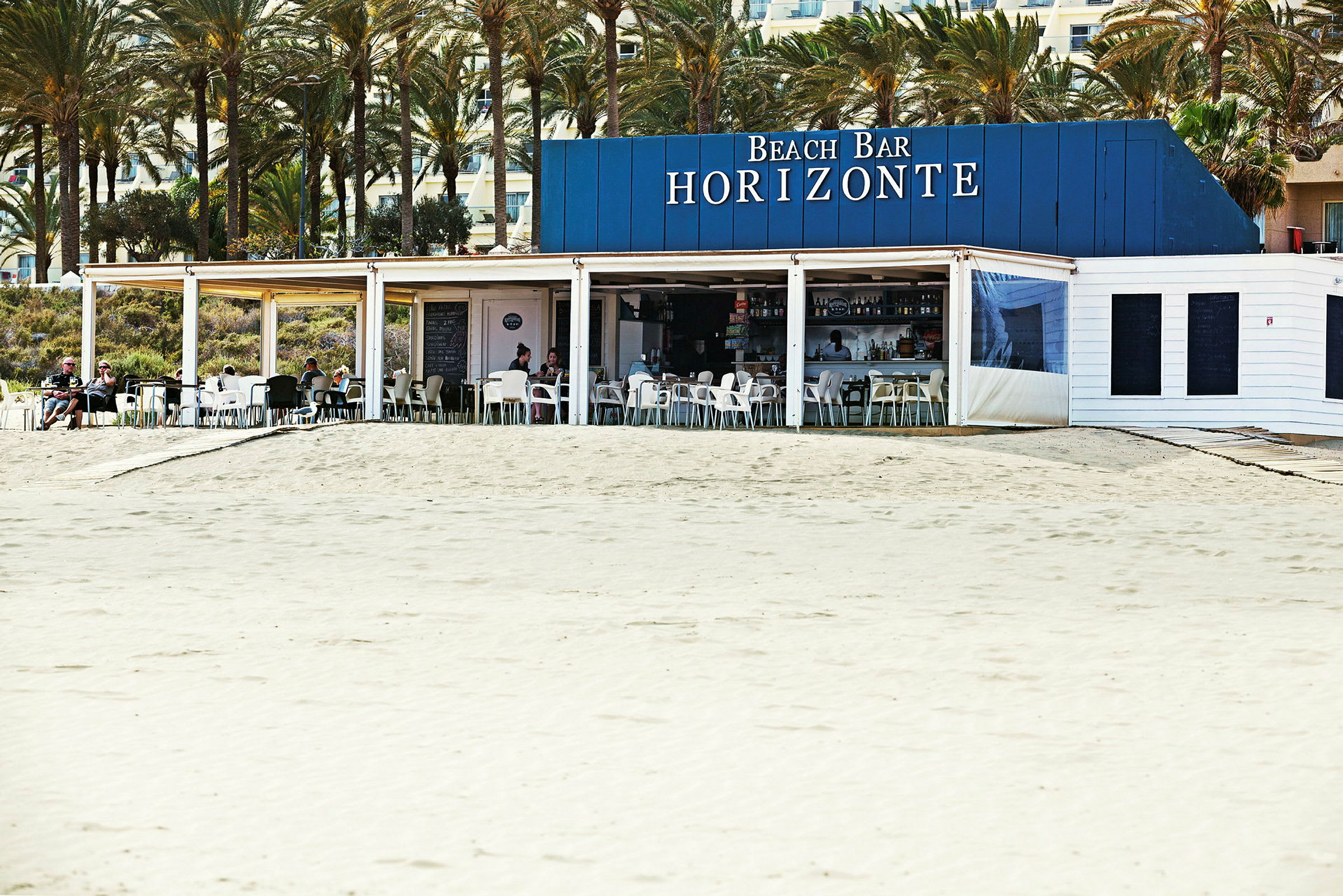 En strandbar med navnet Horizonte, plassert nær en sandstrand og omgitt av palmer. (AI-generert tekst)