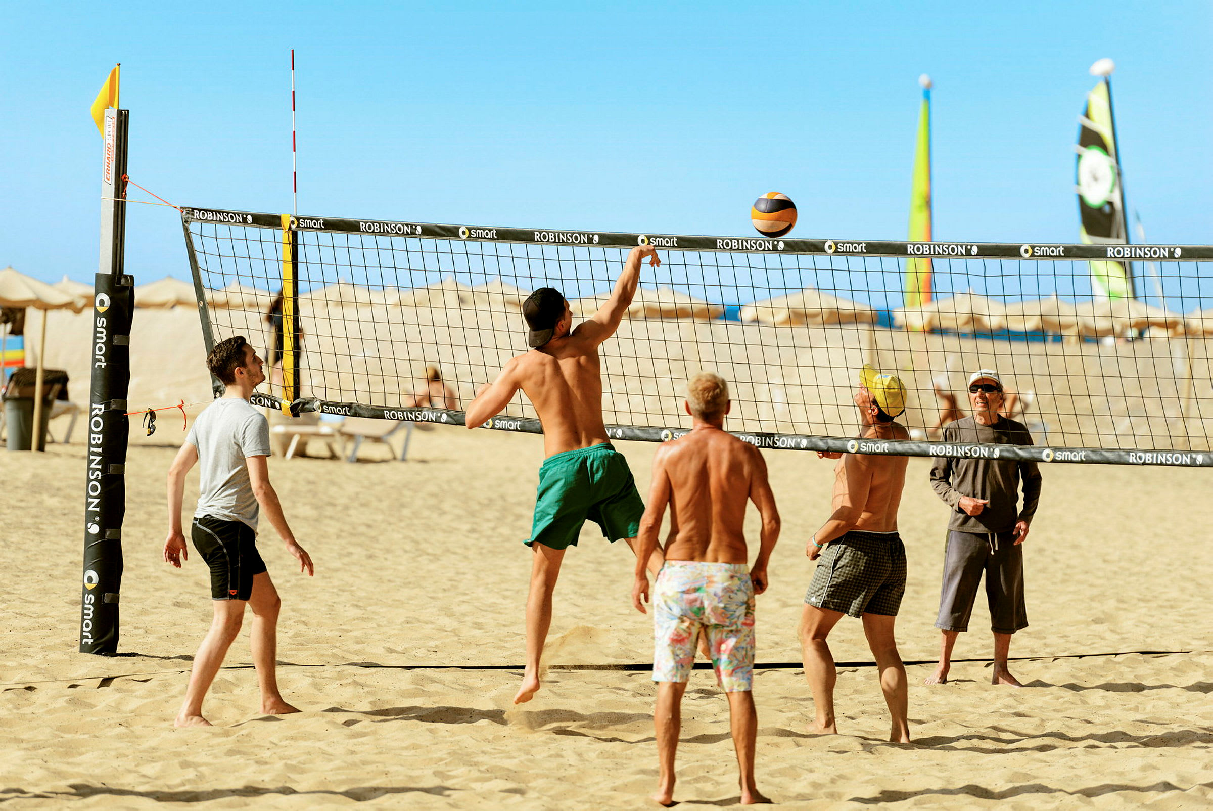 En gruppe mennesker spiller sandvolleyball på en sandstrand under en klar blå himmel. (AI-generert tekst)