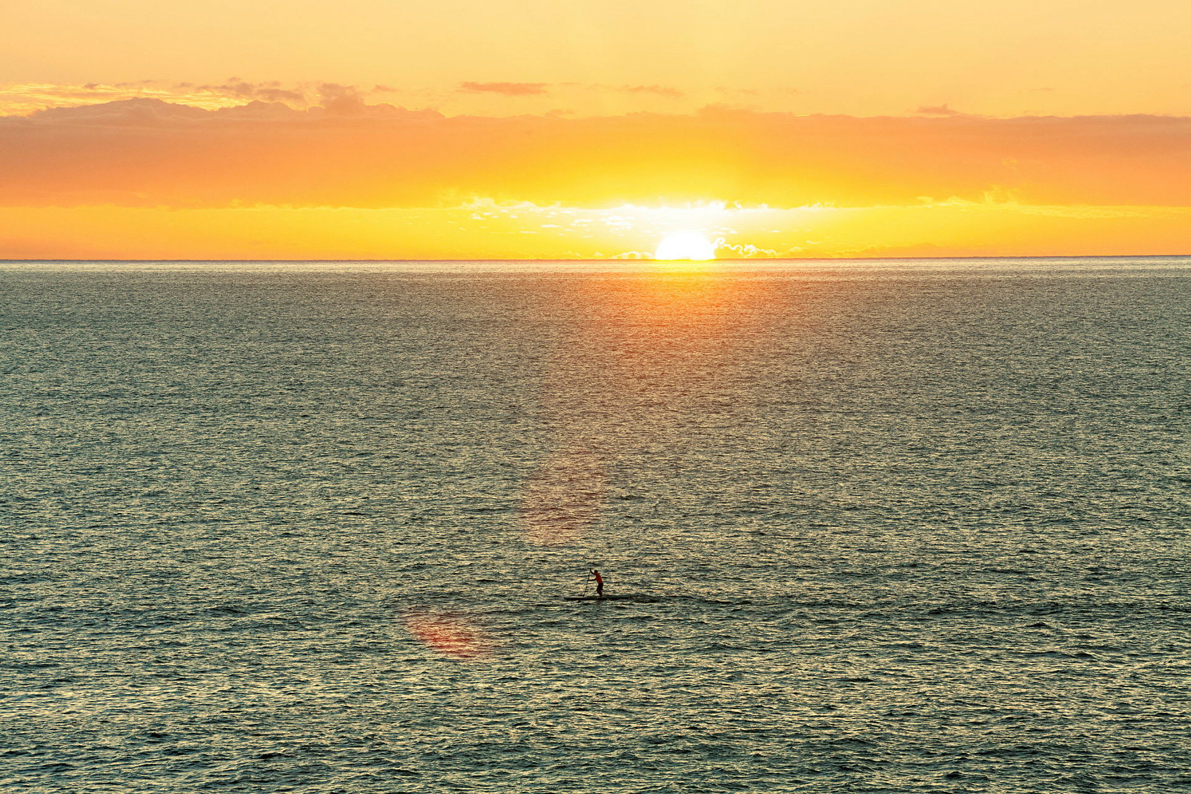 En solnedgang over havet med en person som står og padler på et brett. (AI-generert tekst)