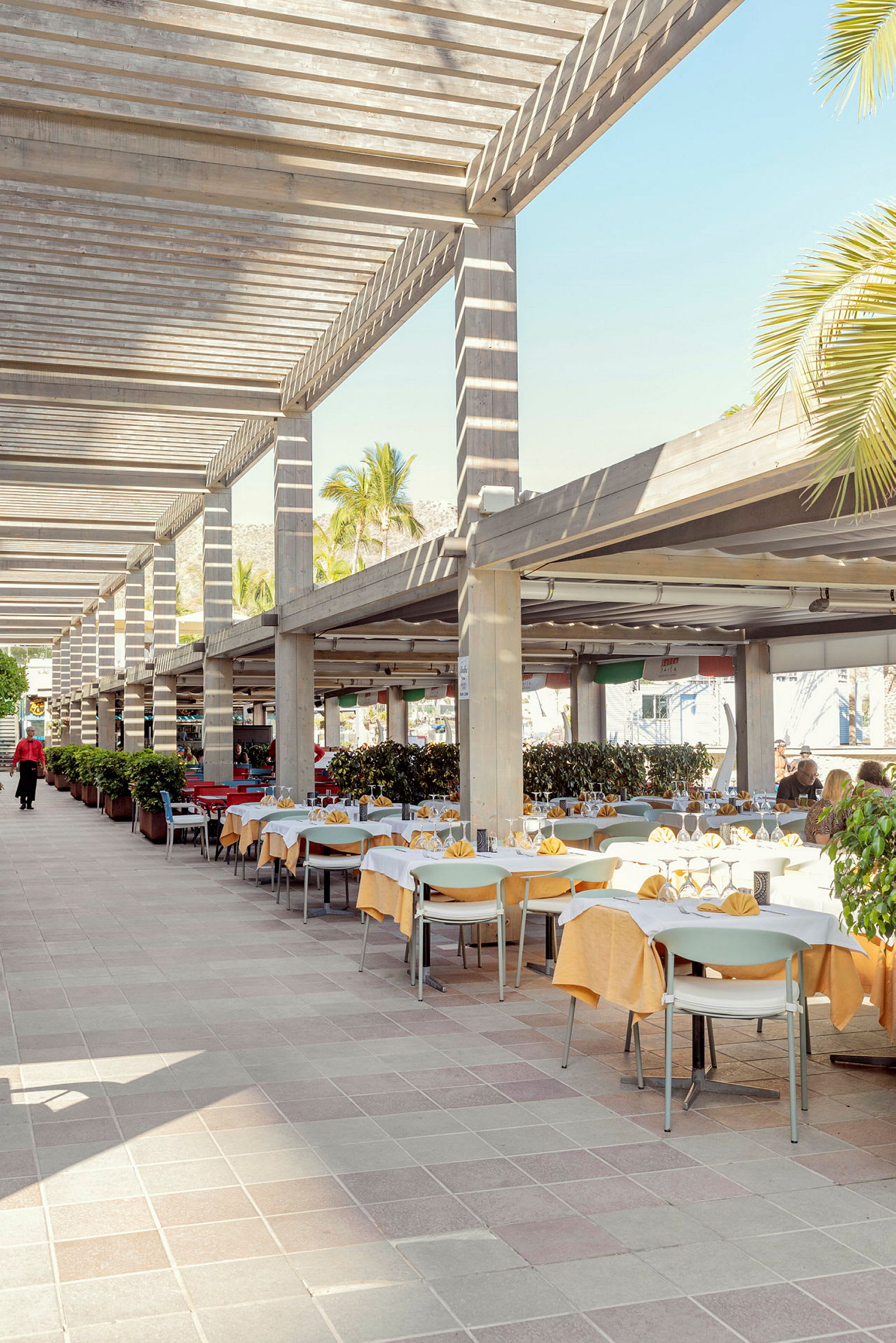 Uteservering med dekkede bord og stoler under pergola. (AI-generert tekst)