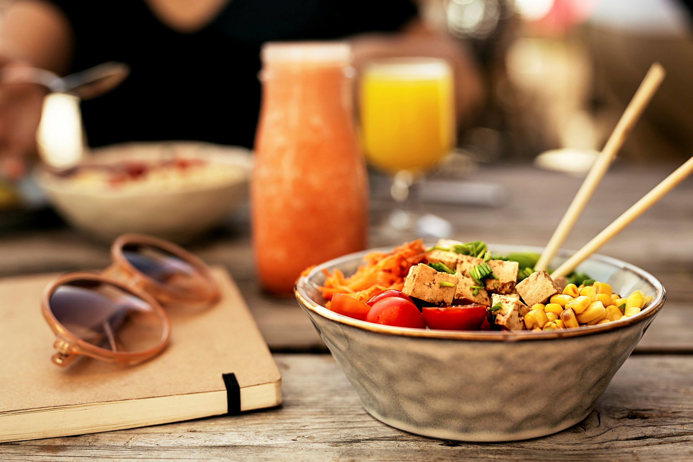 En bolle med salat, et glass med oransje drikk og et glass med gul drikk på et bord. (AI-generert tekst)