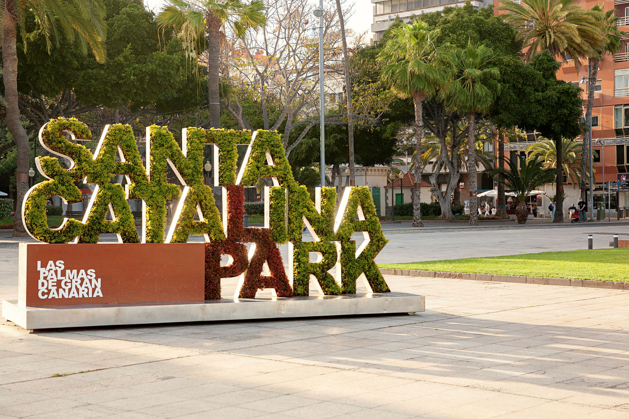 Skilt med teksten 'Santa Catalina Park' fylt med grønt, omgitt av trær i bypark. (AI-generert tekst)