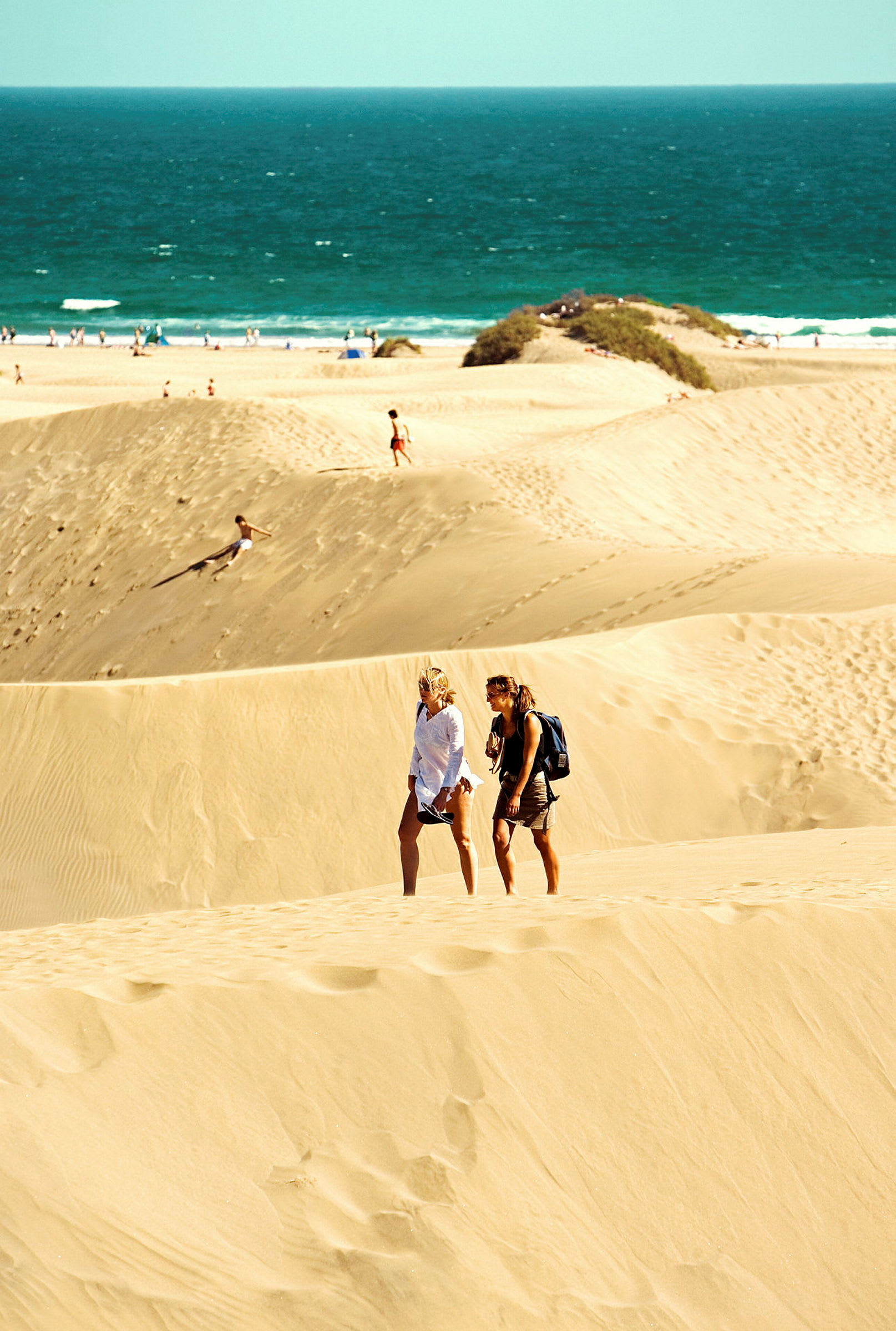 To personer går på sanddyner ved en strand. (AI-generert tekst)