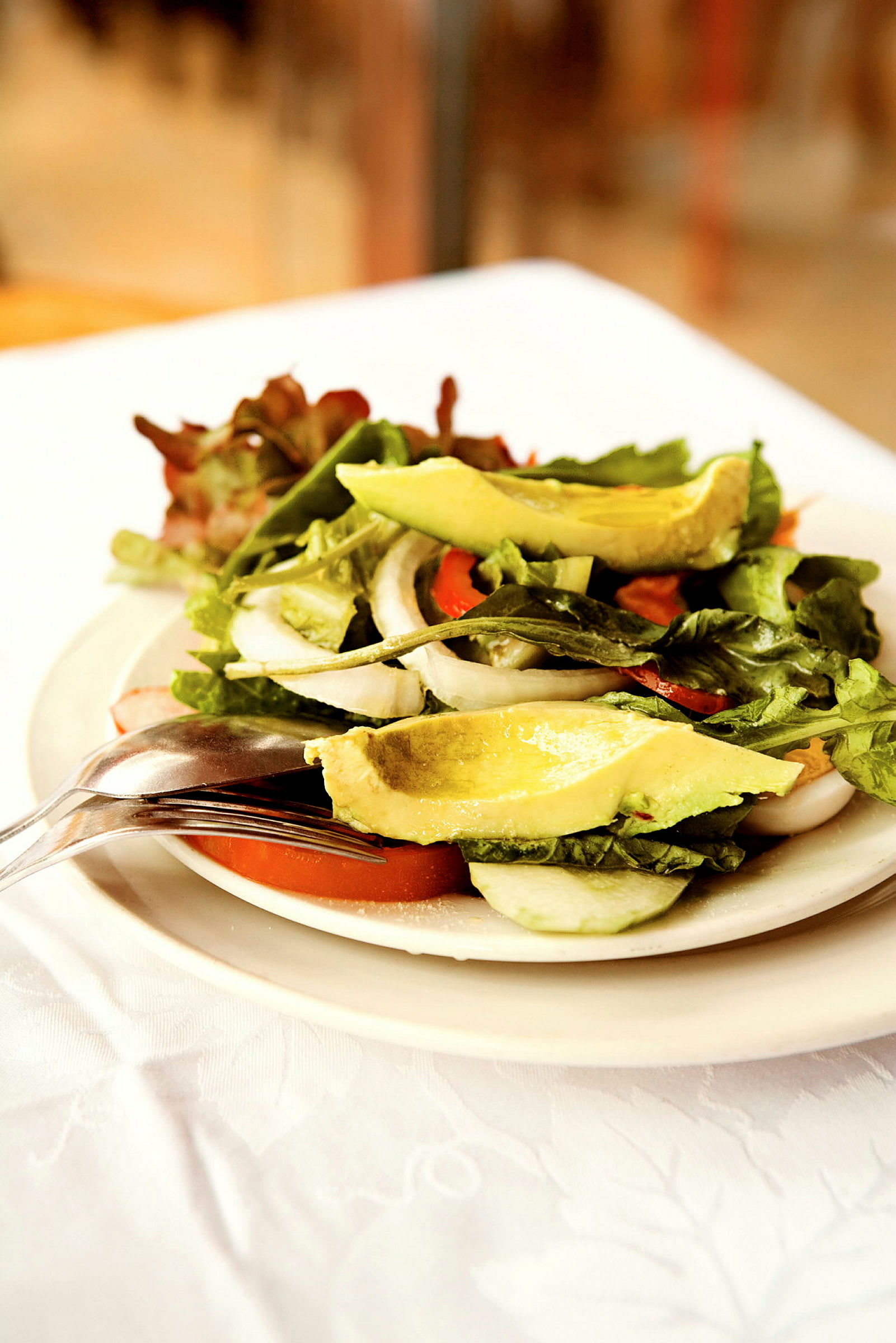 En salat med avokado, tomater, løk og bladsalat servert på en tallerken. (AI-generert tekst)