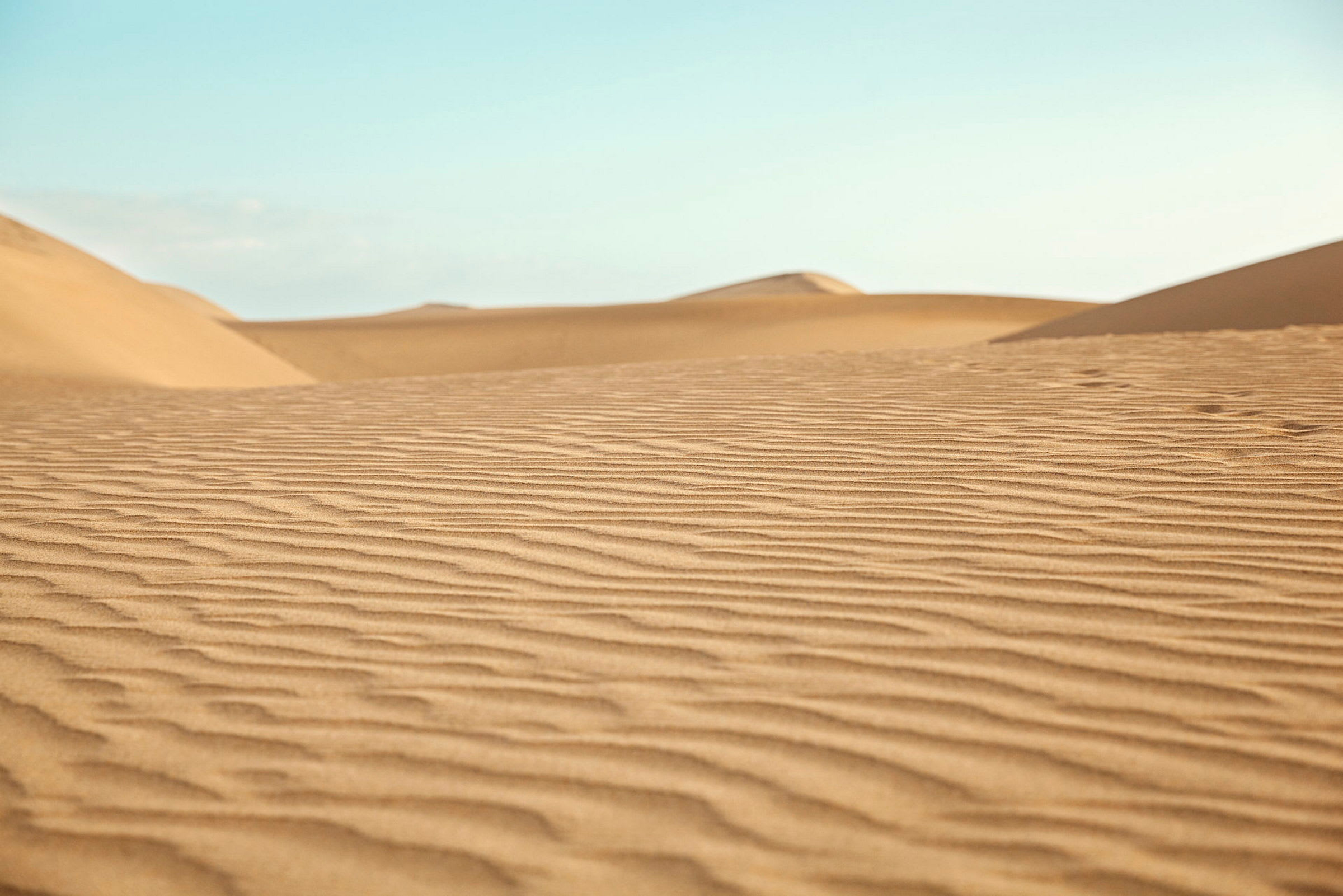 Bilde av sanddyner med finmønstret sand. Klar blå himmel i bakgrunnen. (AI-generert tekst)