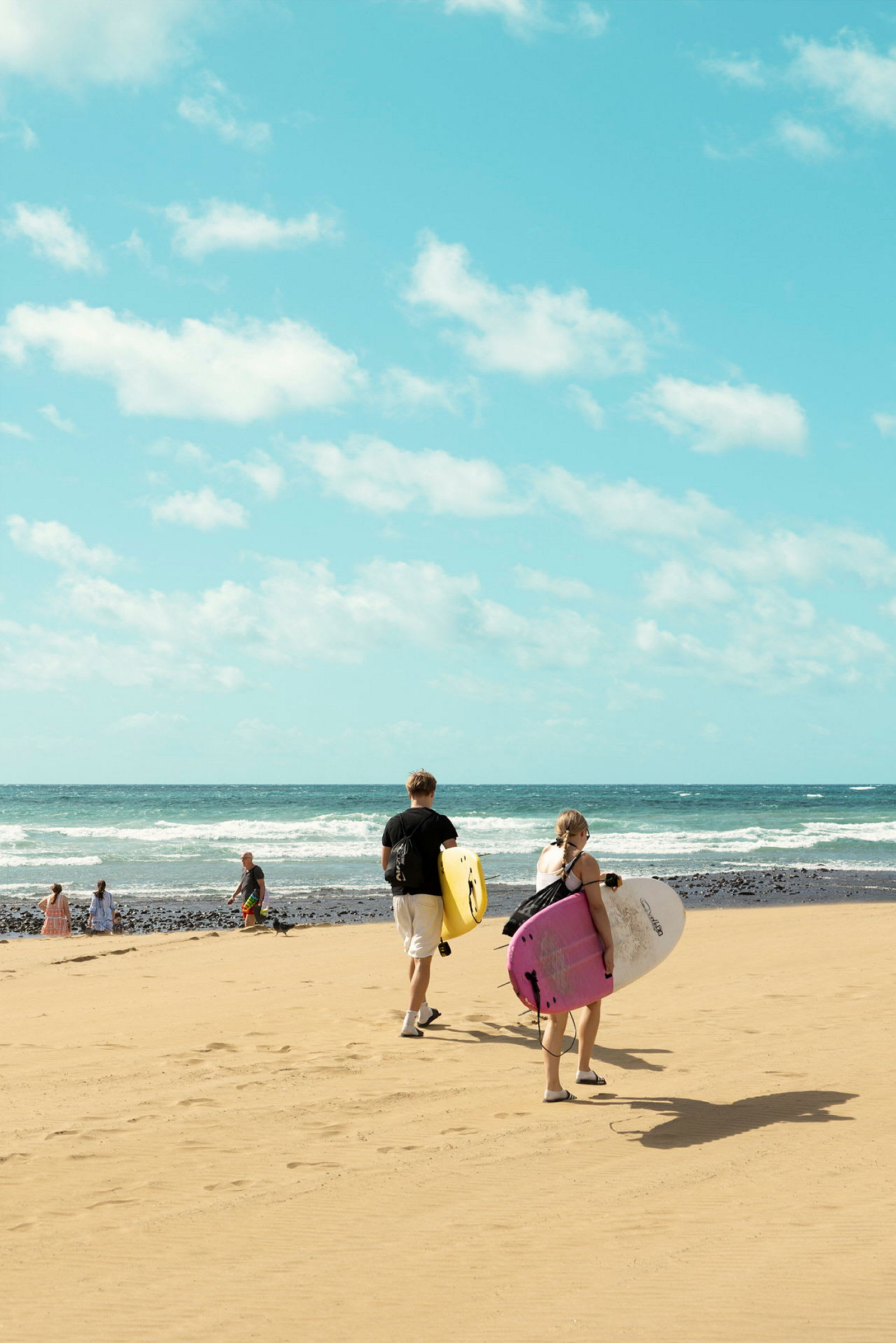 To personer går mot havet på en sandstrand, bærende på surfebrett. (AI-generert tekst)