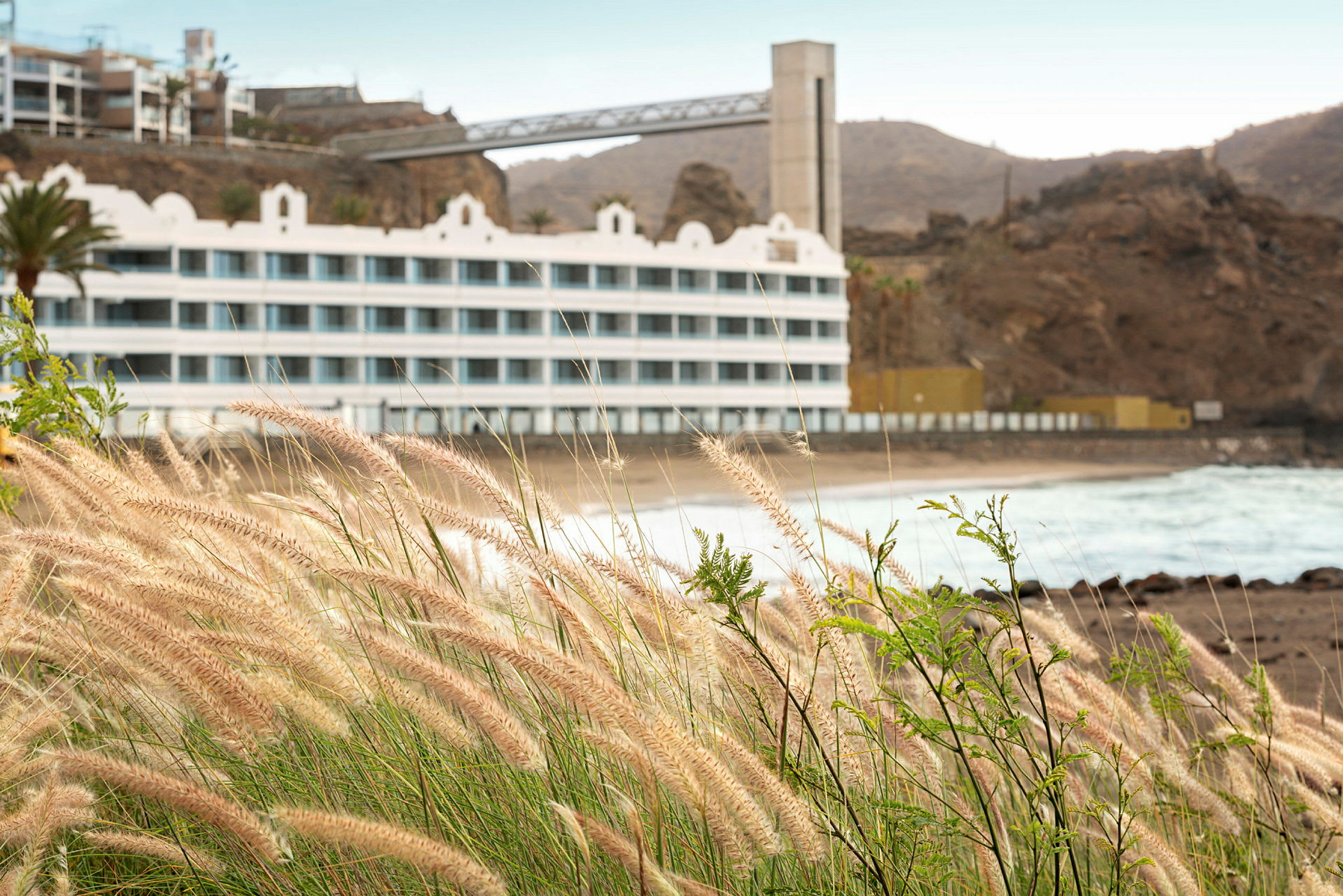 Bilde av et hotell ved en steinete strand med gress i forgrunnen. (AI-generert tekst)