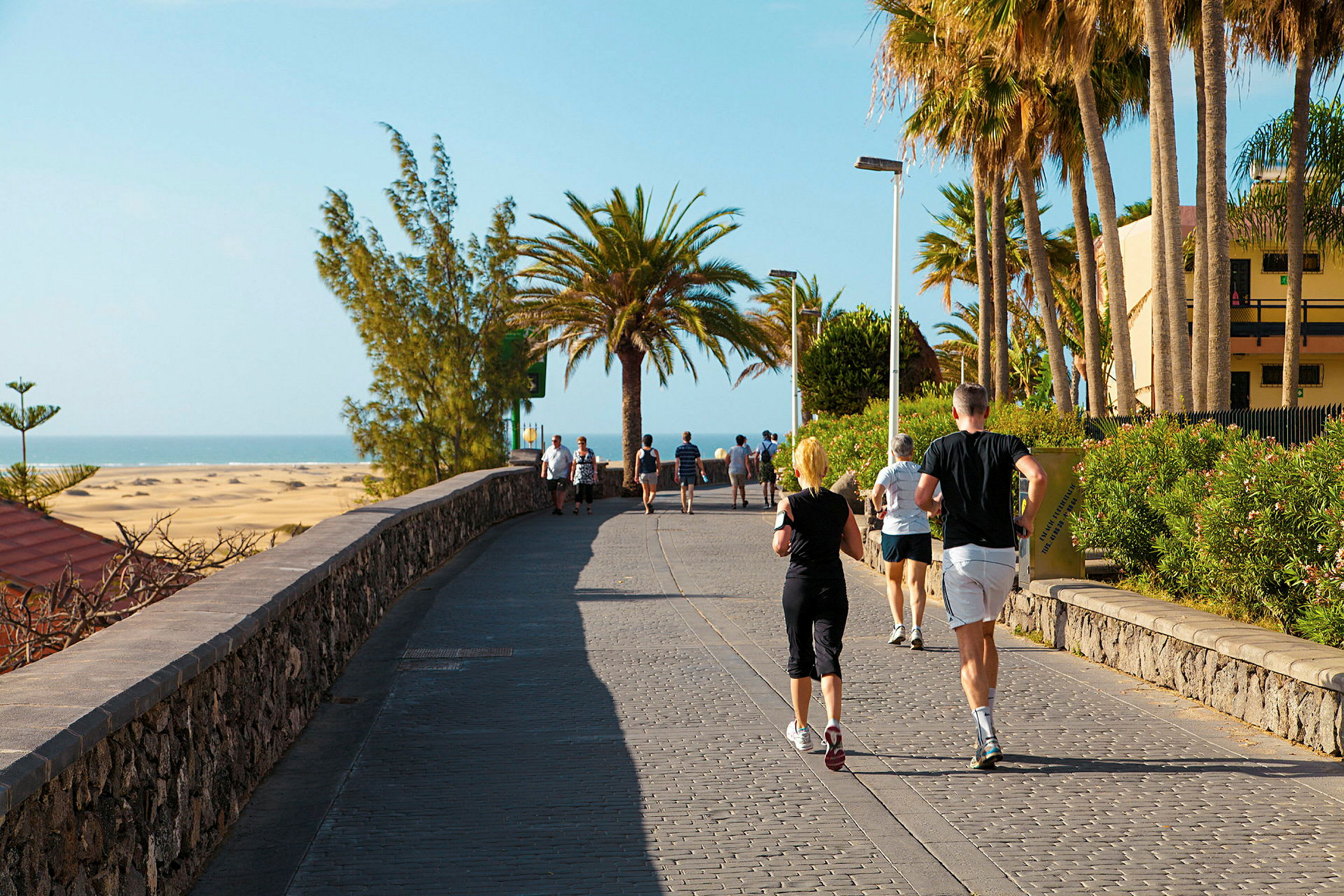 Personer som går og jogger på en gangvei ved stranden. (AI-generert tekst)