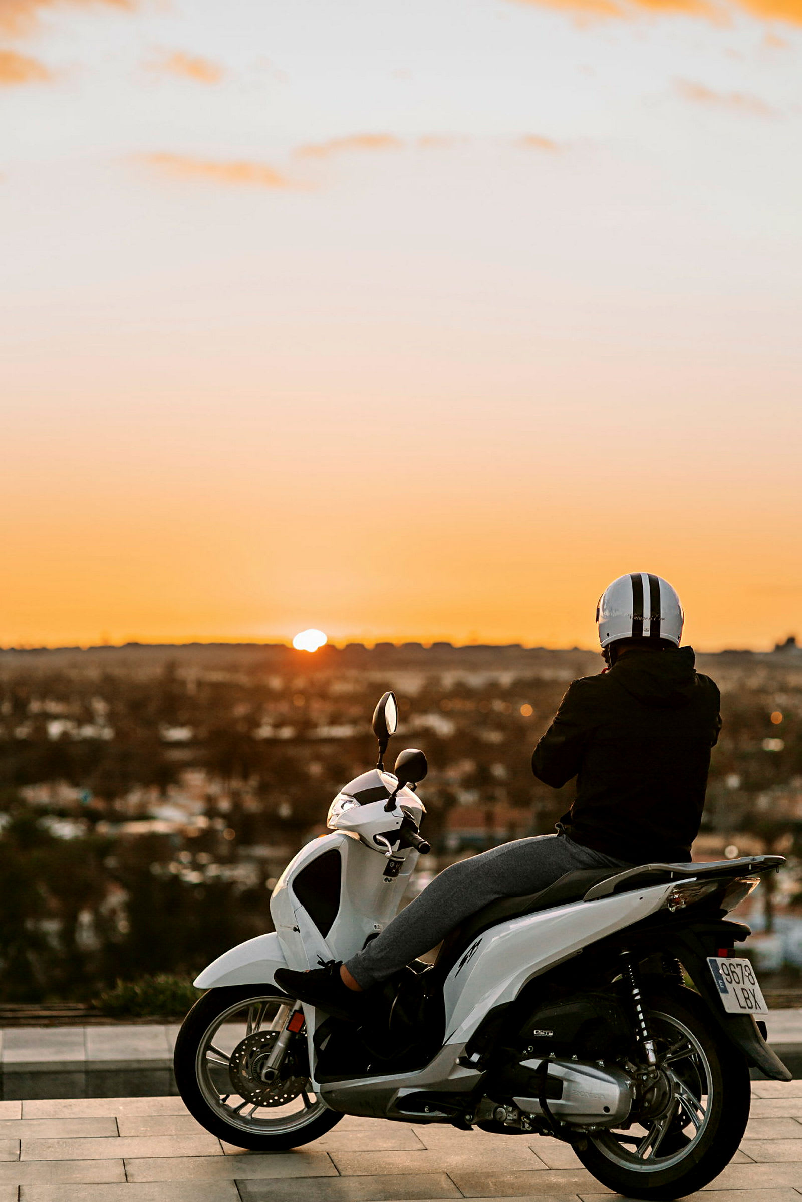 En person sitter på en hvit scooter og ser på solnedgangen. (AI-generert tekst)