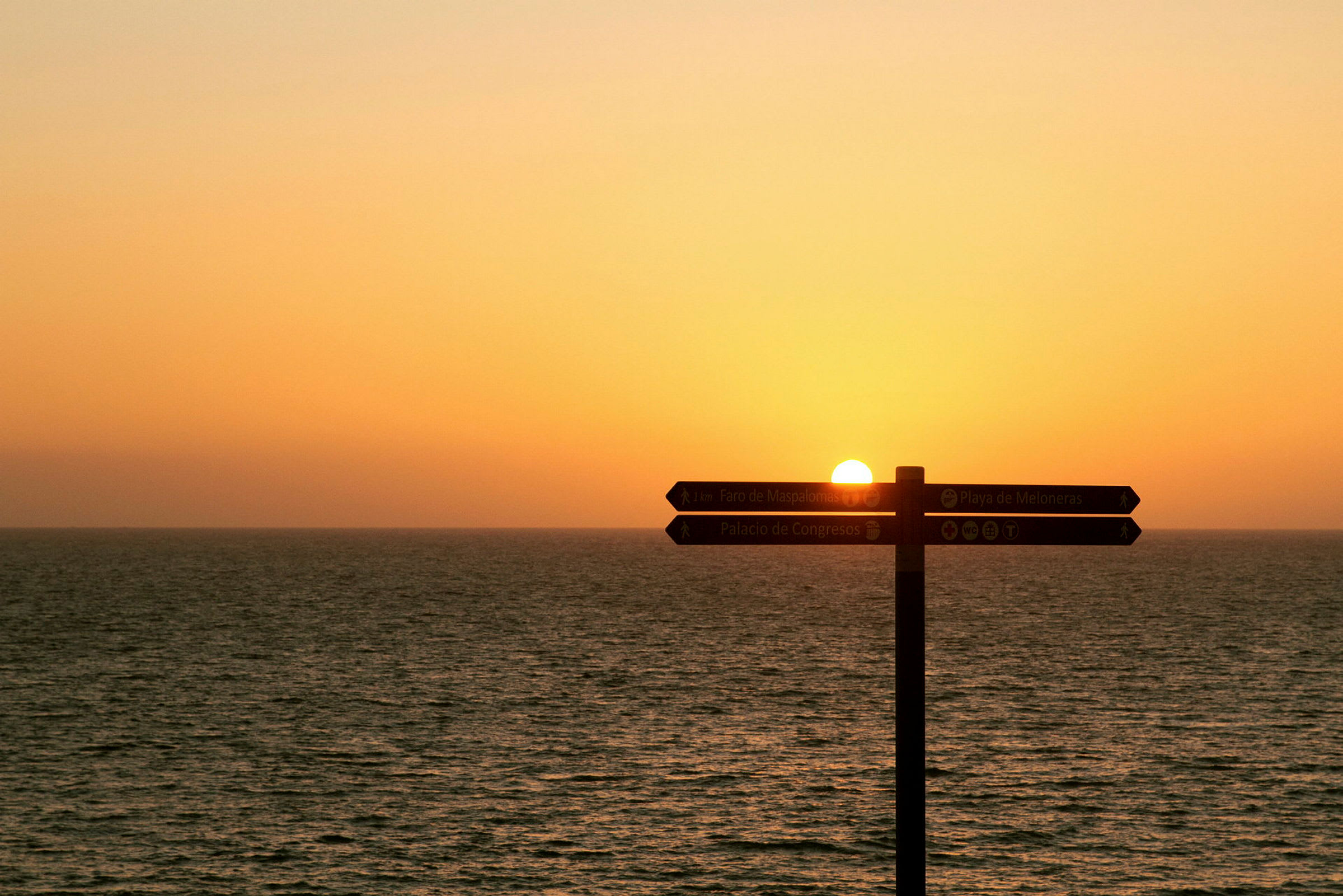 Solnedgang over havet med et veiskilt. (AI-generert tekst)