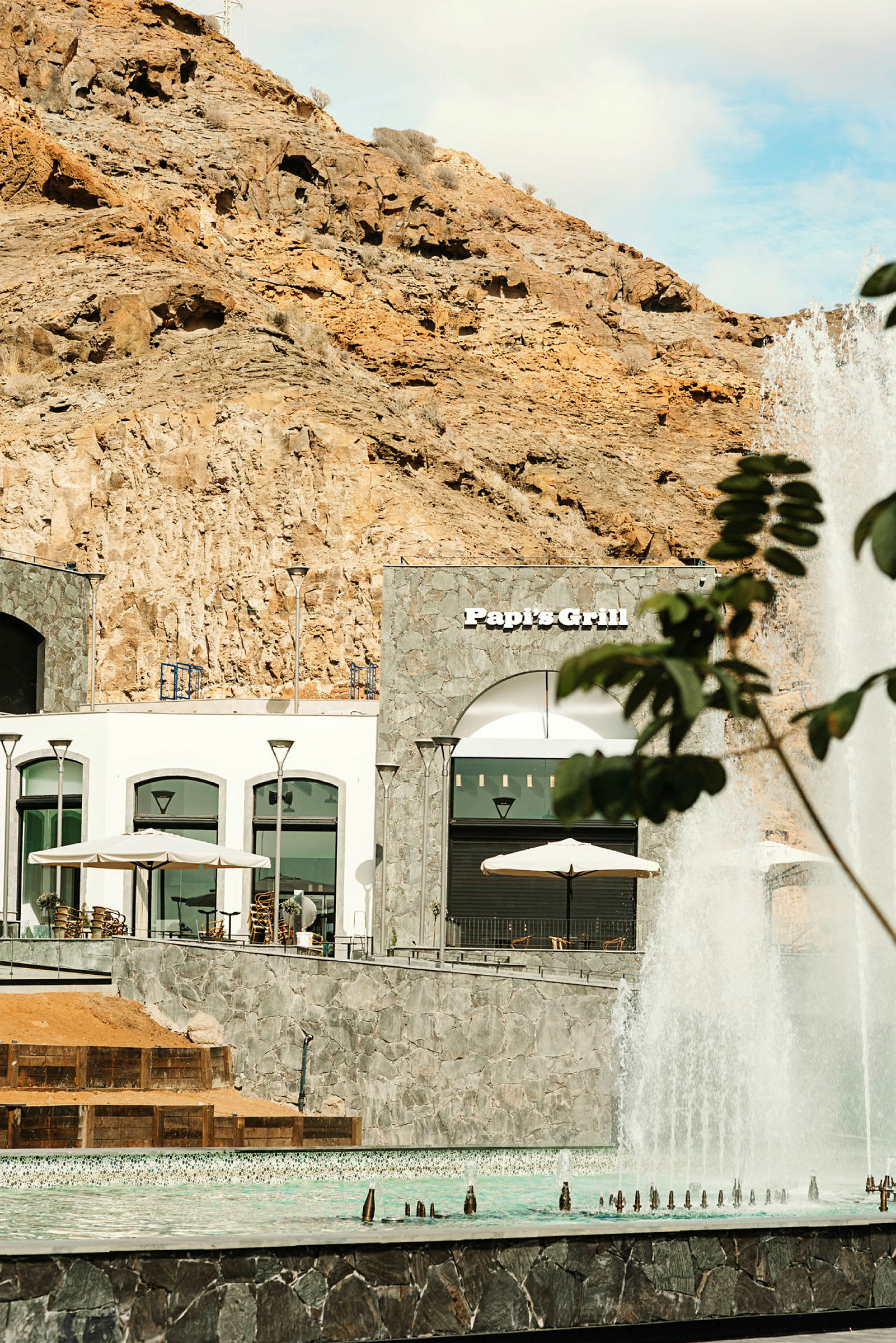 Bilde av en steinfasade med restauranten Papi's Grill, fontene i forgrunnen. (AI-generert tekst)
