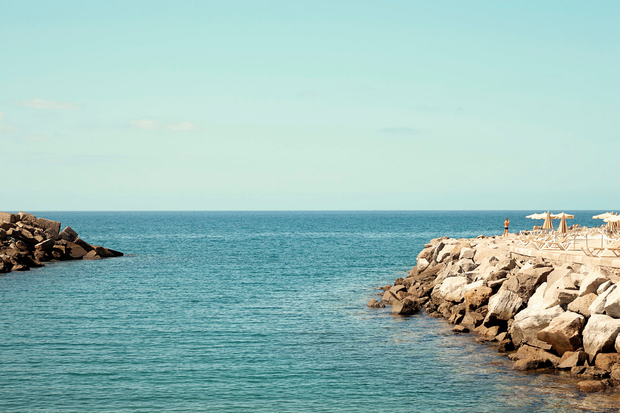 Utsikt over havet med steinete kyst og solsenger under parasoller. (AI-generert tekst)