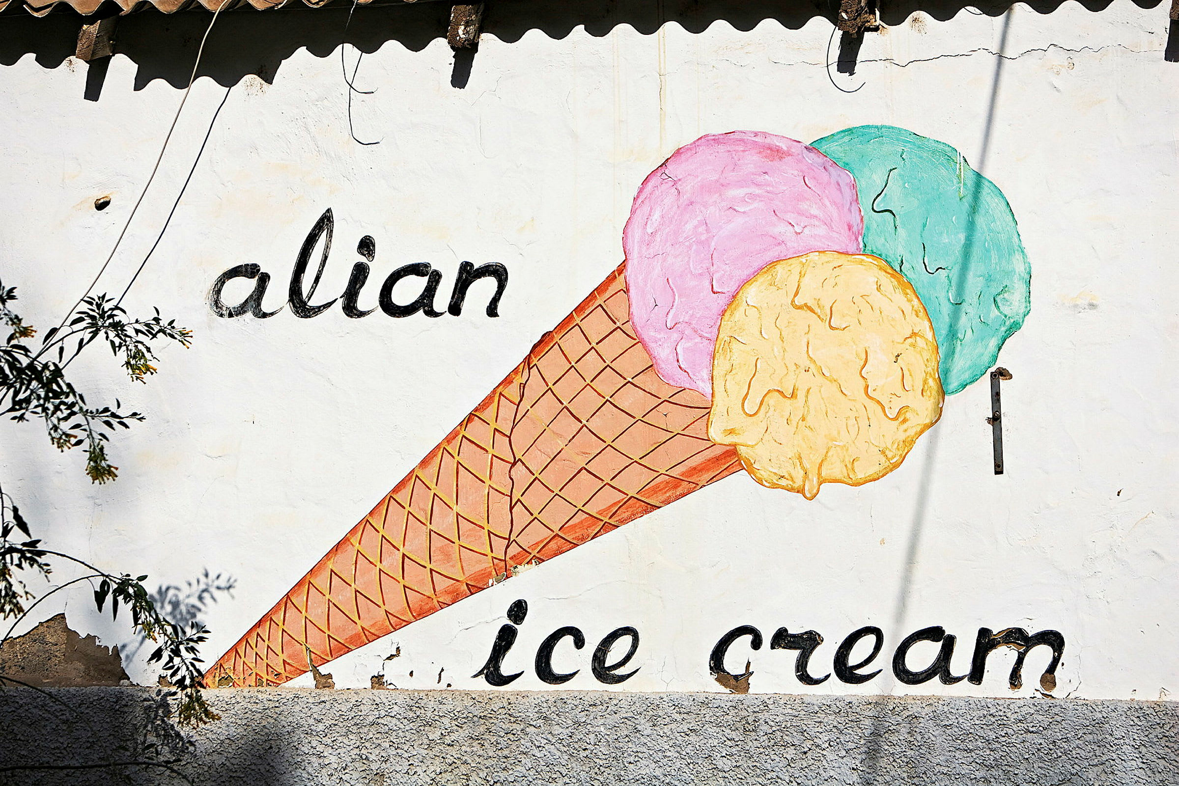 Maling av en iskremkjeks med tre fargerike kuler på en vegg med teksten 'alian ice cream'. (AI-generert tekst)