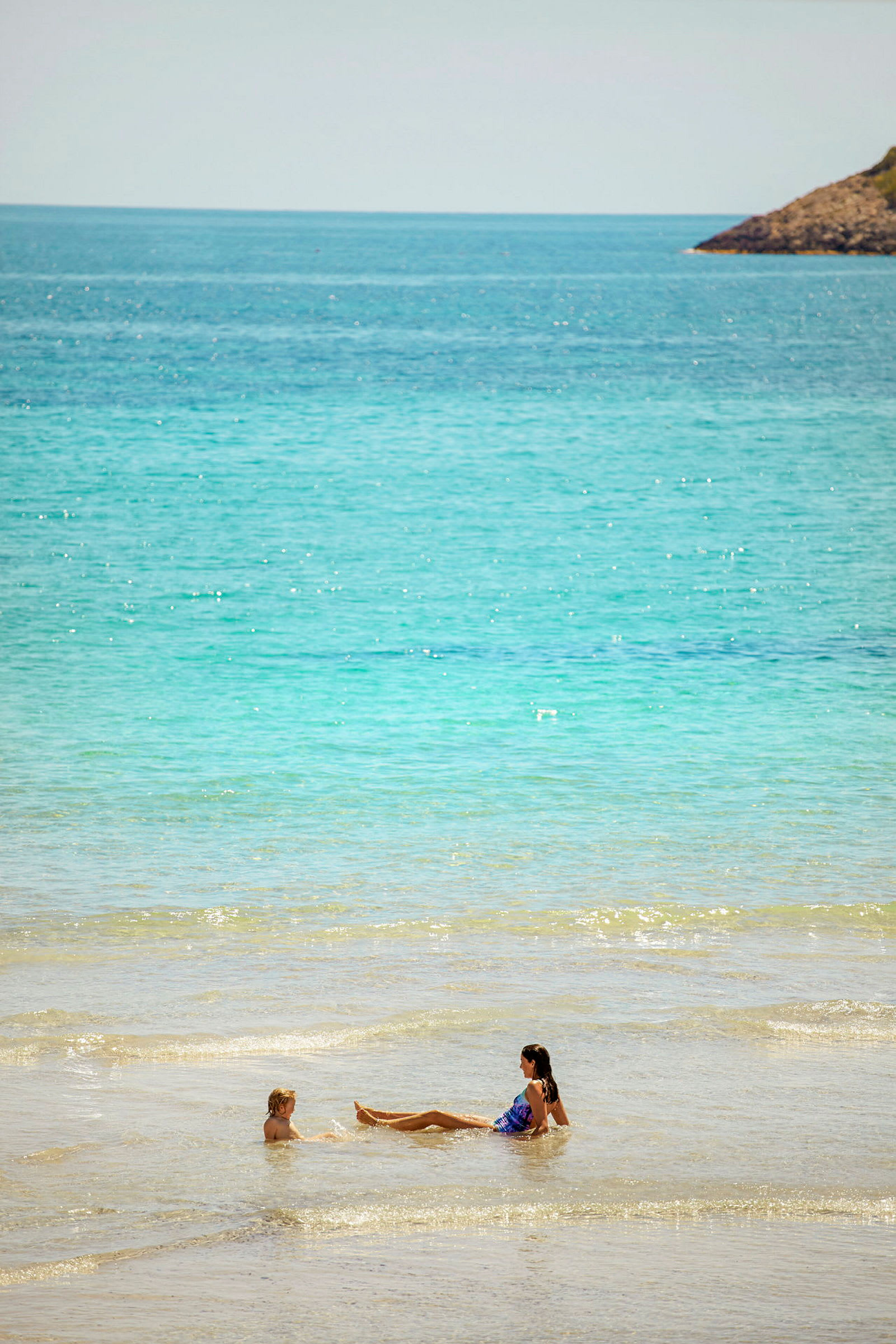 To personer bader i grunt klart vann ved en strand. (AI-generert tekst)