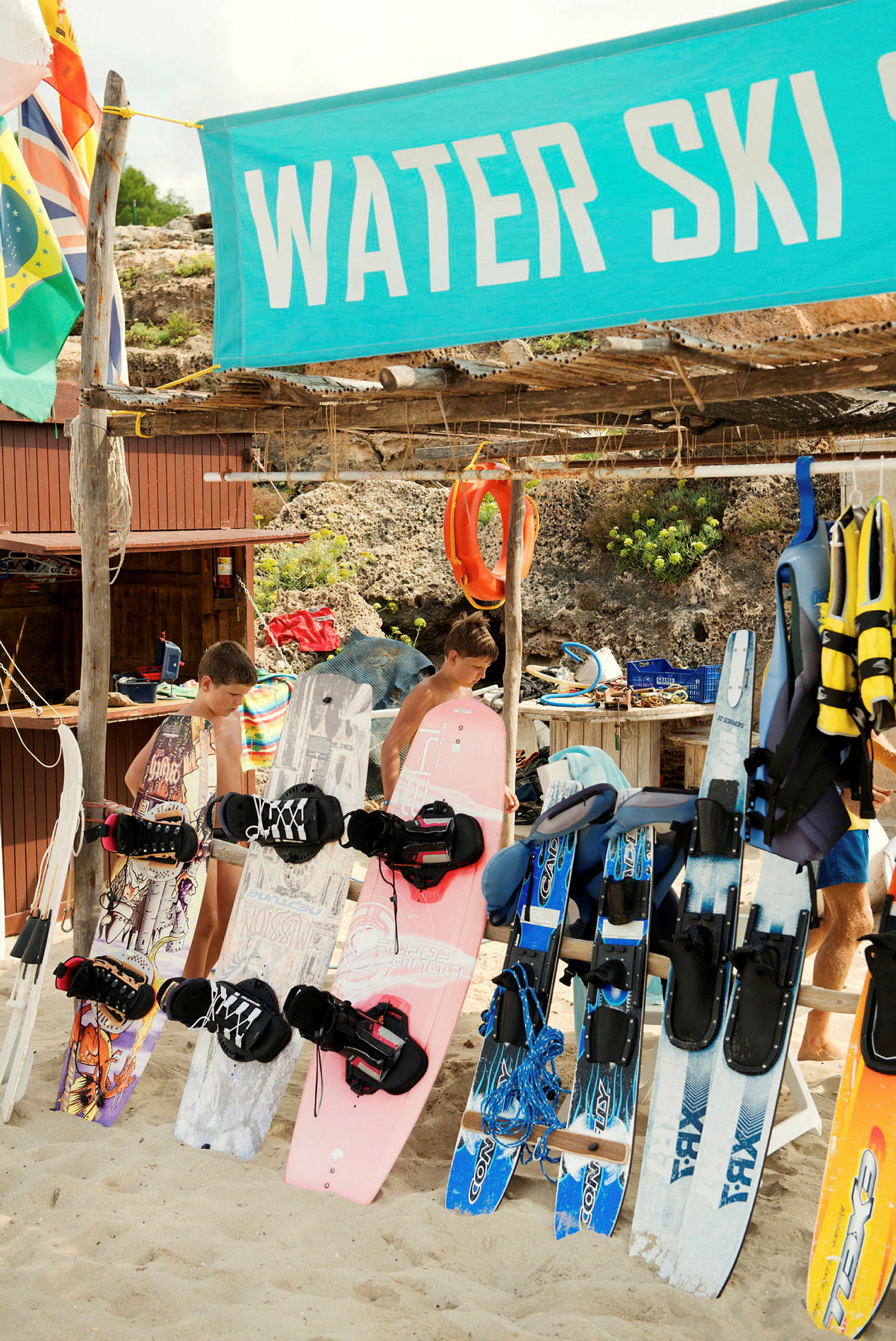 Et utvalg av vannsportutstyr, inkludert wakeboard og vannski, er utstilt på en strand nær et skilt som sier "Water Ski". (AI-generert tekst)