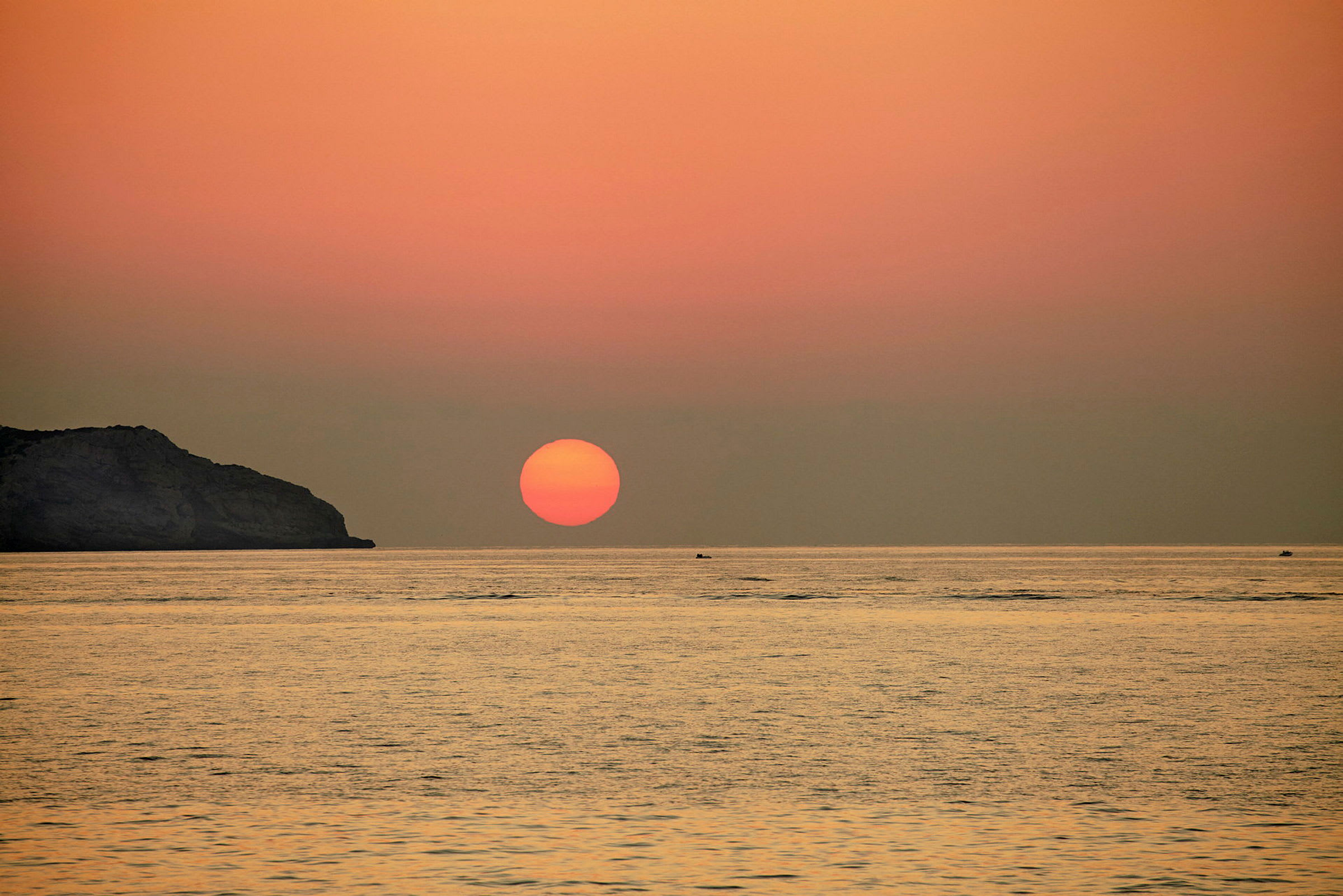 Bilde av en solnedgang over havet med en klippeformasjon til venstre. (AI-generert tekst)