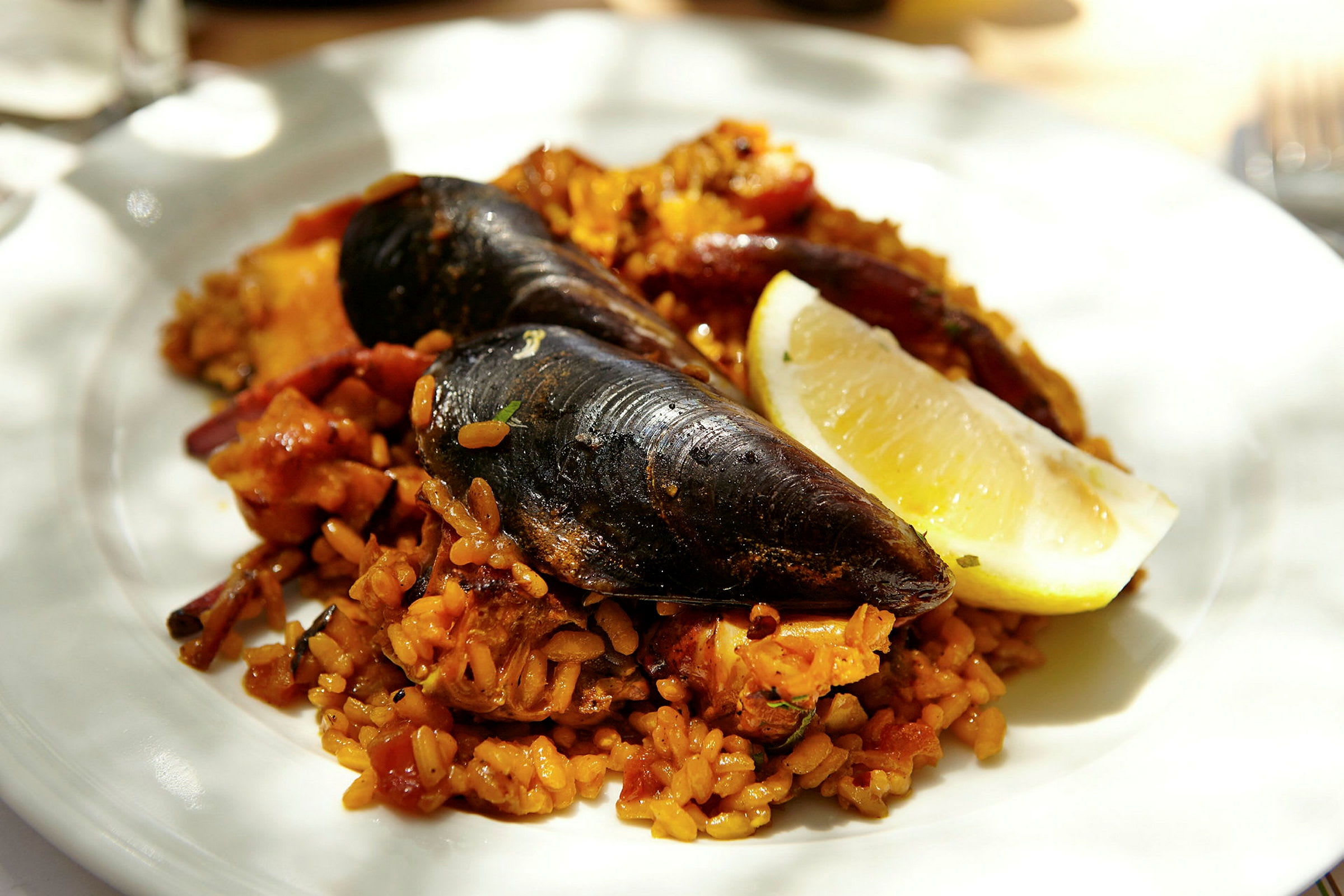 En tallerken med paella som inneholder blåskjell, krydret ris og en sitronskive. (AI-generert tekst)