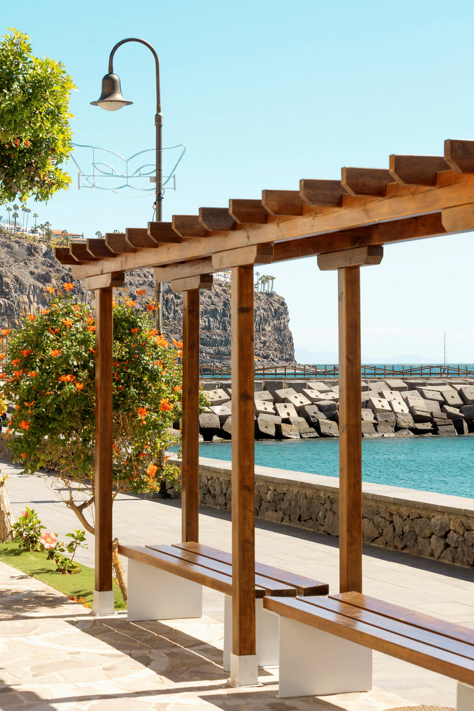 Trelastpergola med benk ved sjøen. (AI-generert tekst)