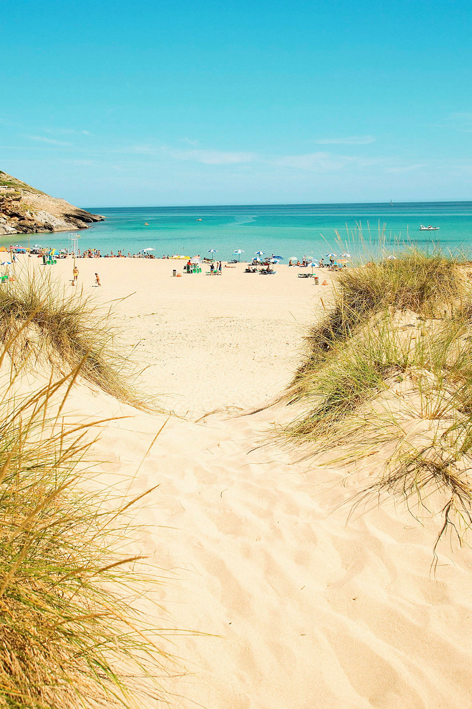 Utsikt fra en sandstrand med havet i bakgrunnen, hvor mennesker og parasoller er synlige på avstand. (AI-generert tekst)