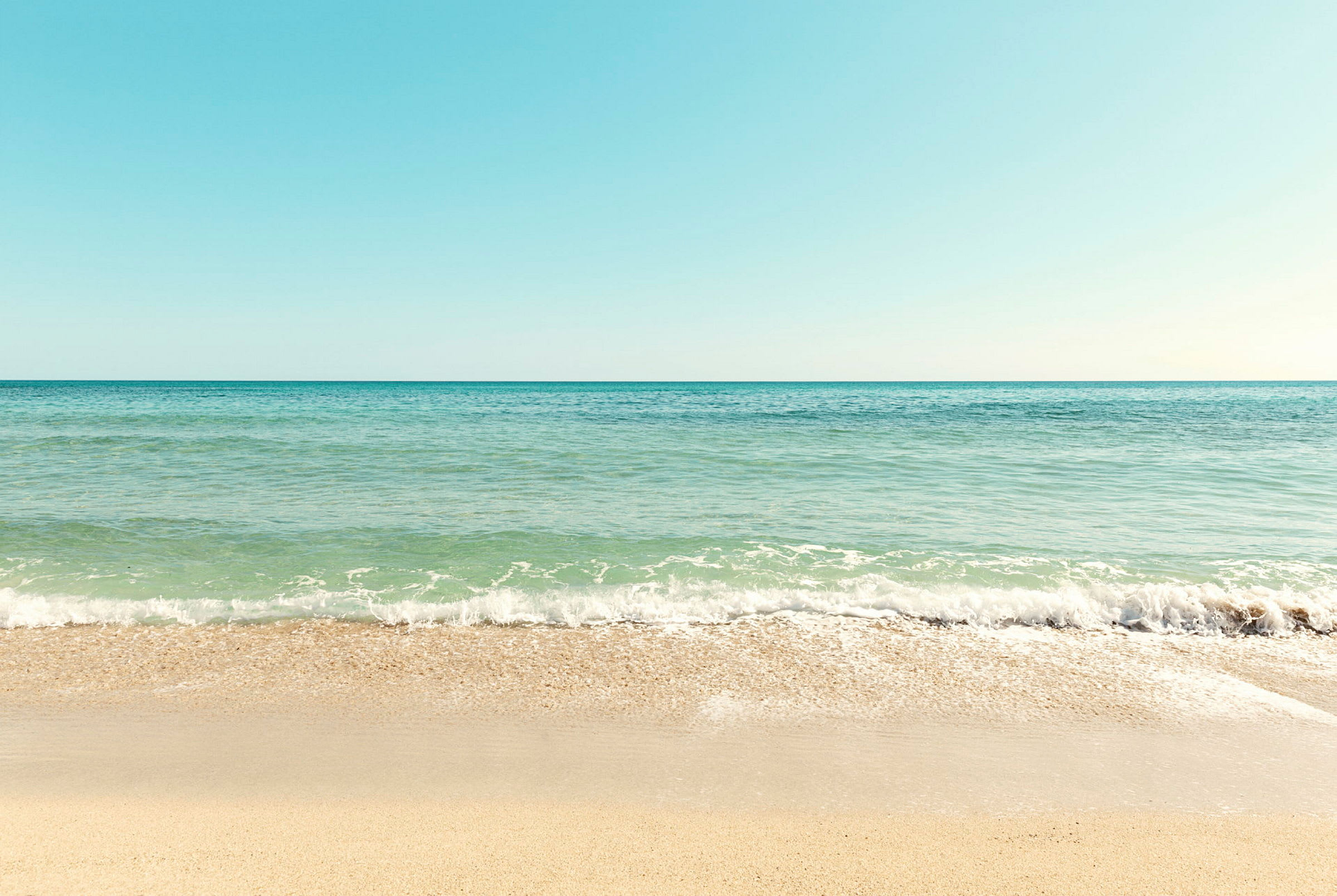 En strand med sand og havet som møter himmelen. (AI-generert tekst)