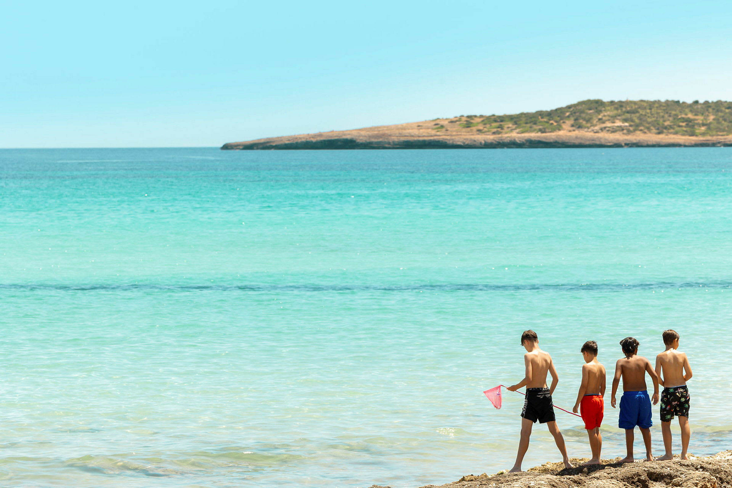 Fire barn står på stranden og ser utover havet. (AI-generert tekst)