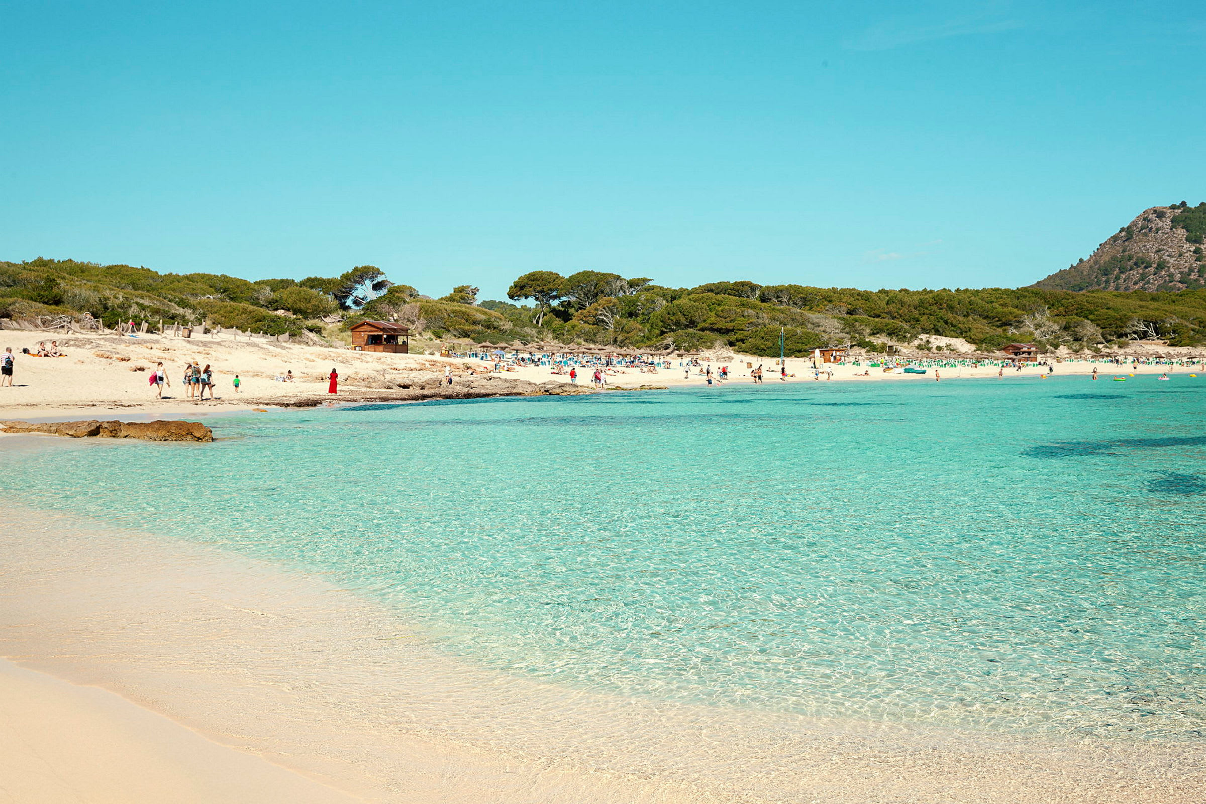 En strand med klart vann og mennesker som nyter solen. (AI-generert tekst)