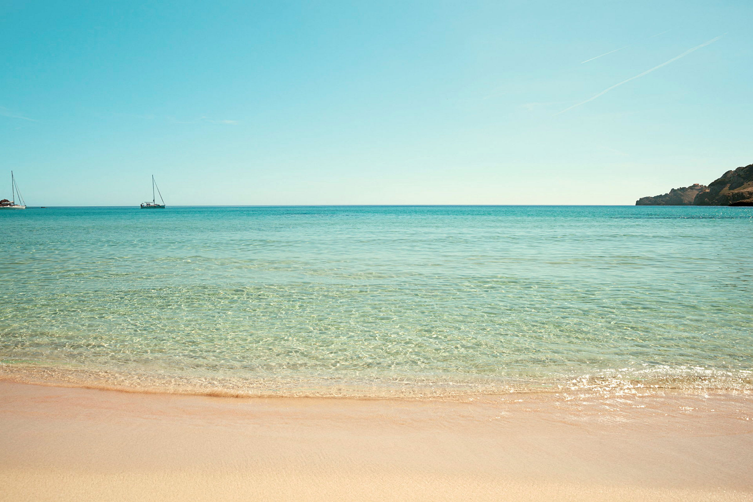 Strand med klart vann og to seilbåter i havet. (AI-generert tekst)