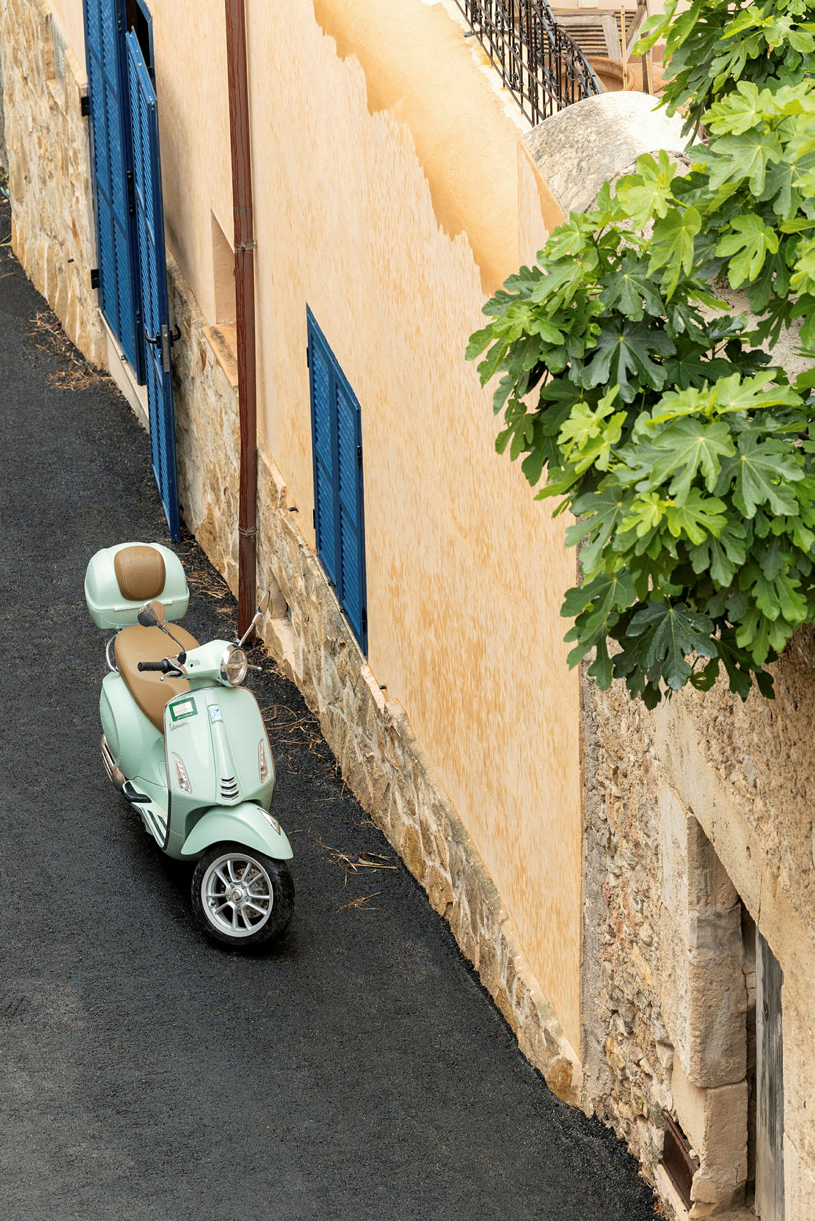 En lys grønn scooter står parkert ved en beige bygning med blå trevinduslemmer. (AI-generert tekst)