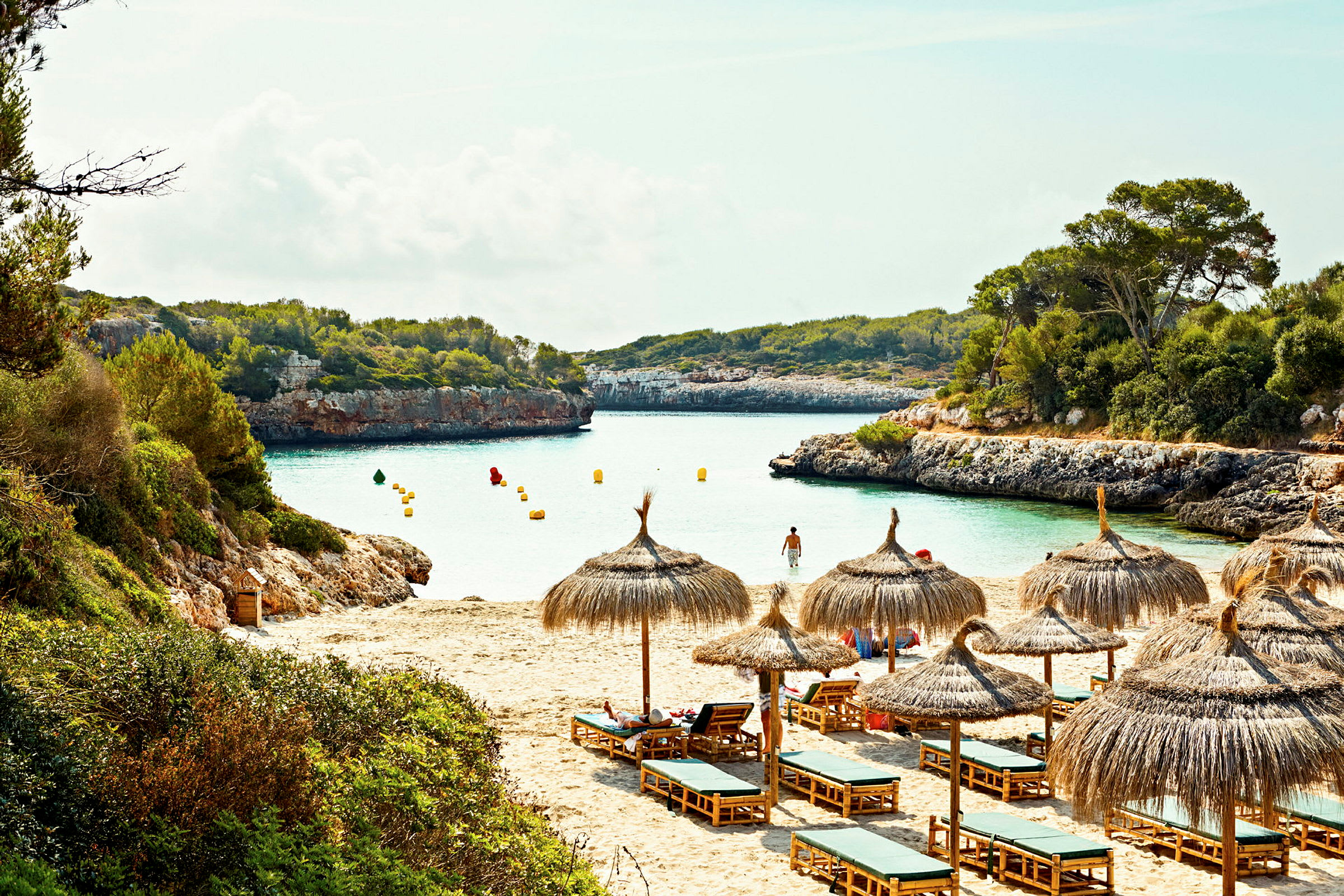 En strand med parasoller og solsenger ved en bukt med klart vann. (AI-generert tekst)