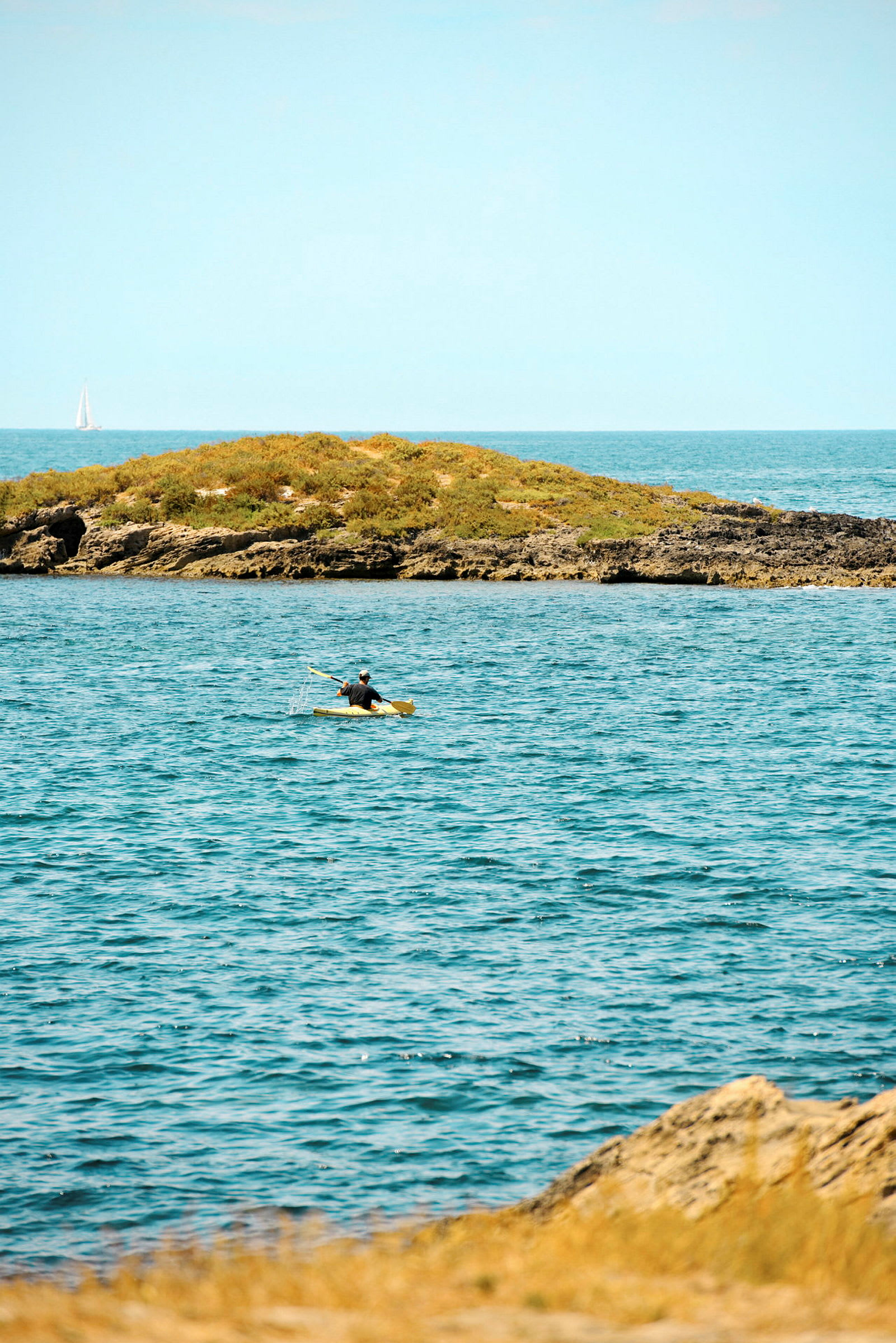 En person padler kajakk på havet nær en liten grønn øy. (AI-generert tekst)