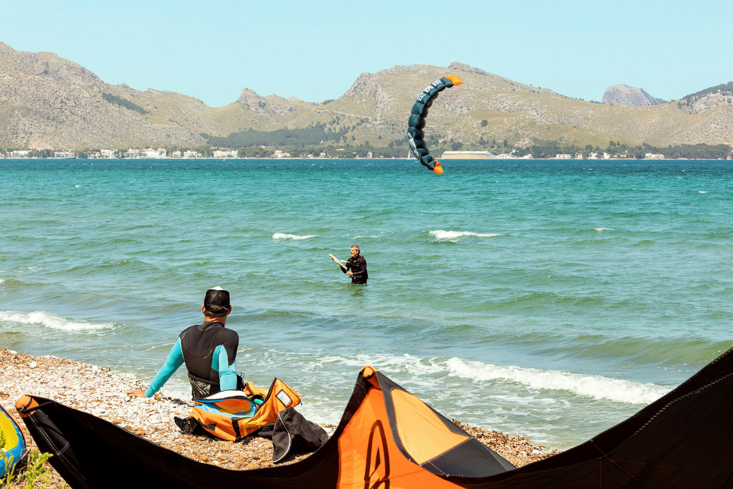 Person som driver med kitesurfing nær strandkanten, med fjell i bakgrunnen. (AI-generert tekst)