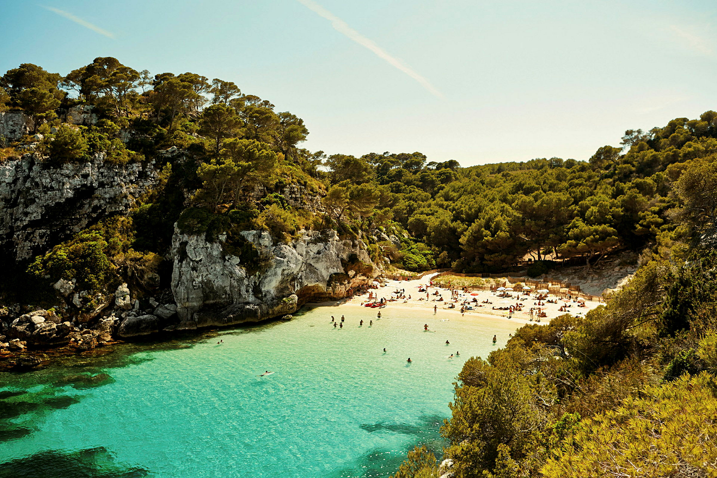 En liten bukt med en strand og turkis vann omgitt av klipper og skog. (AI-generert tekst)