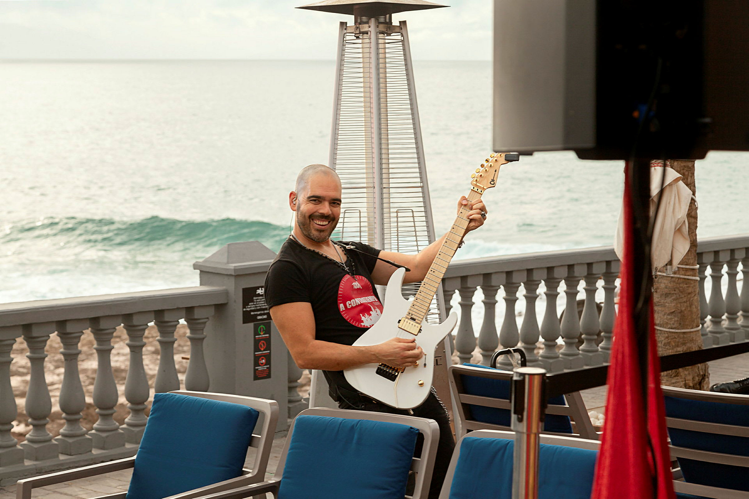 Person spiller elektrisk gitar ved en uteservering med havet i bakgrunnen. (AI-generert tekst)