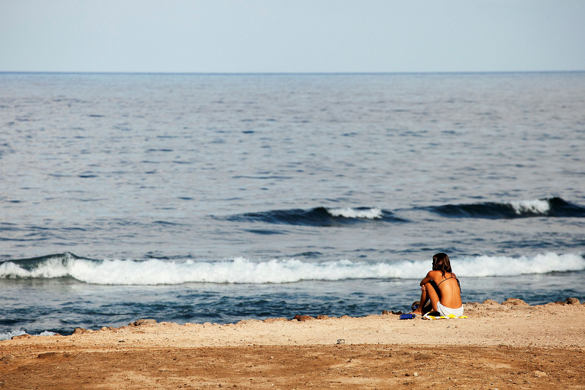 En person sitter på en strand ved havet. (AI-generert tekst)