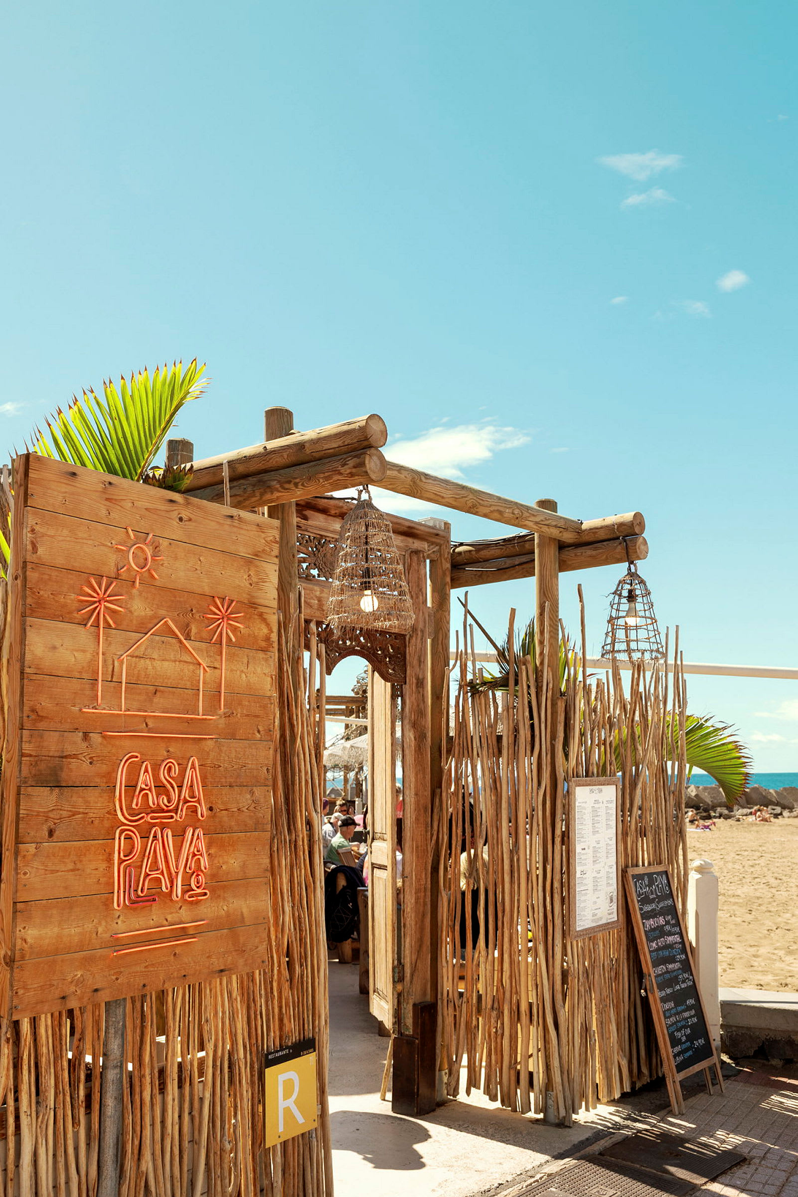 En strandrestaurant med trekonstruksjon og neonskilt som sier 'Casa Playa'. (AI-generert tekst)