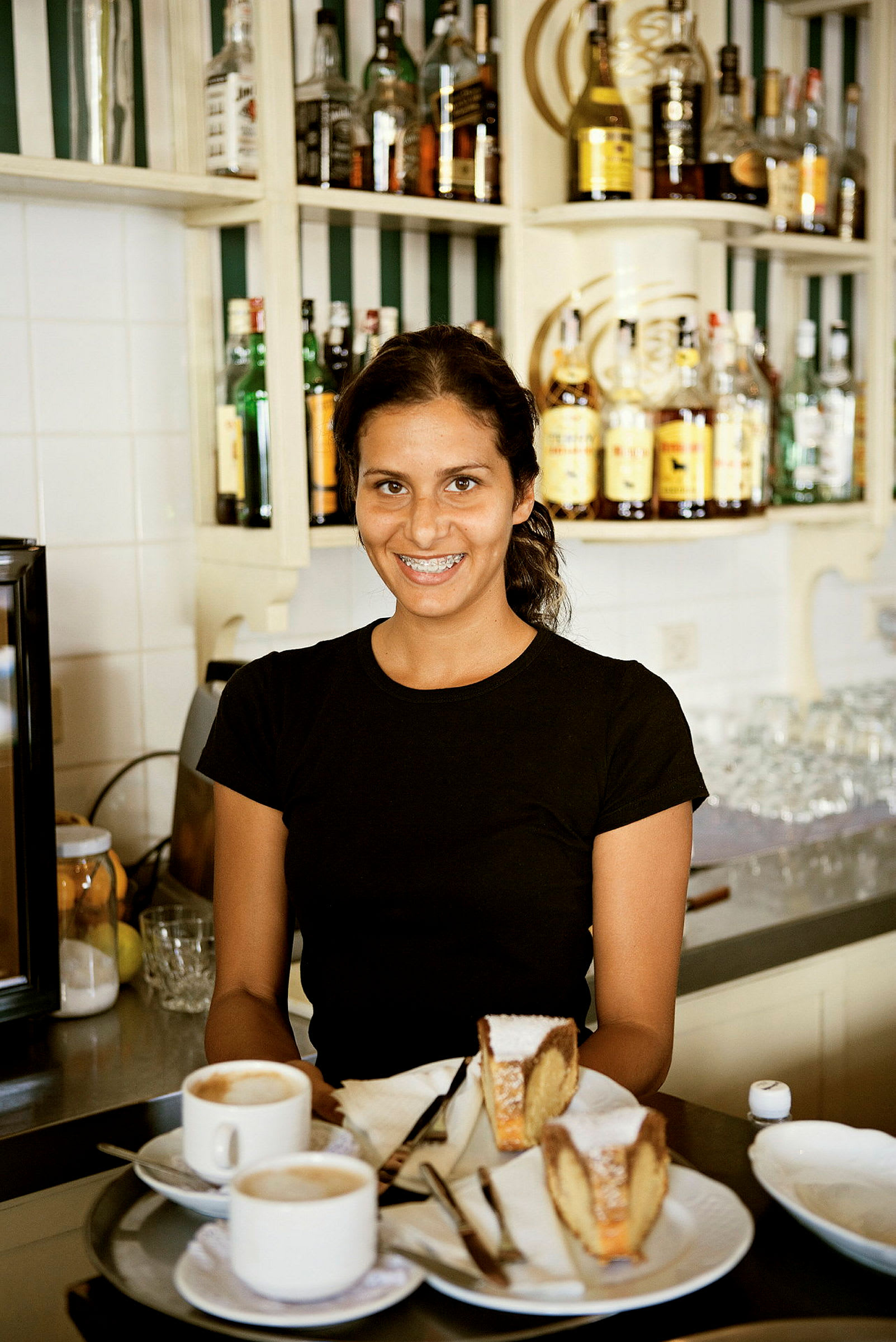 Et serveringsbrett med to kopper kaffe og to kakestykker plassert på et bord foran en bar. (AI-generert tekst)