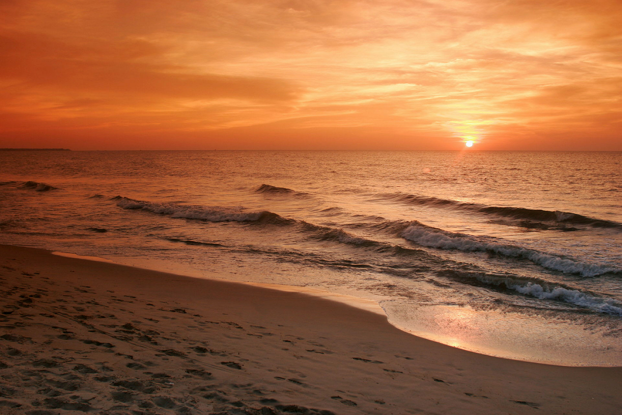 Bilde som viser en strand ved havet med bølger og en solnedgang. (AI-generert tekst)